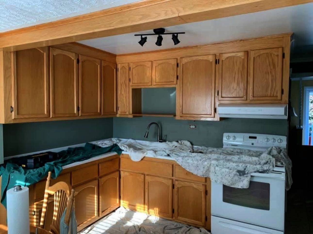 A kitchen with natural wood cabinets, a white stove, a dark green backsplash, and a wooden support beam overhead.