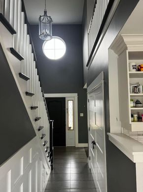 A high-ceilinged foyer with a dark staircase, a circular window, a hanging lantern, and white-trimmed paneling.