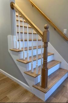 A staircase with light wood steps, white risers, white vertical balusters, and a wooden handrail and newel post.