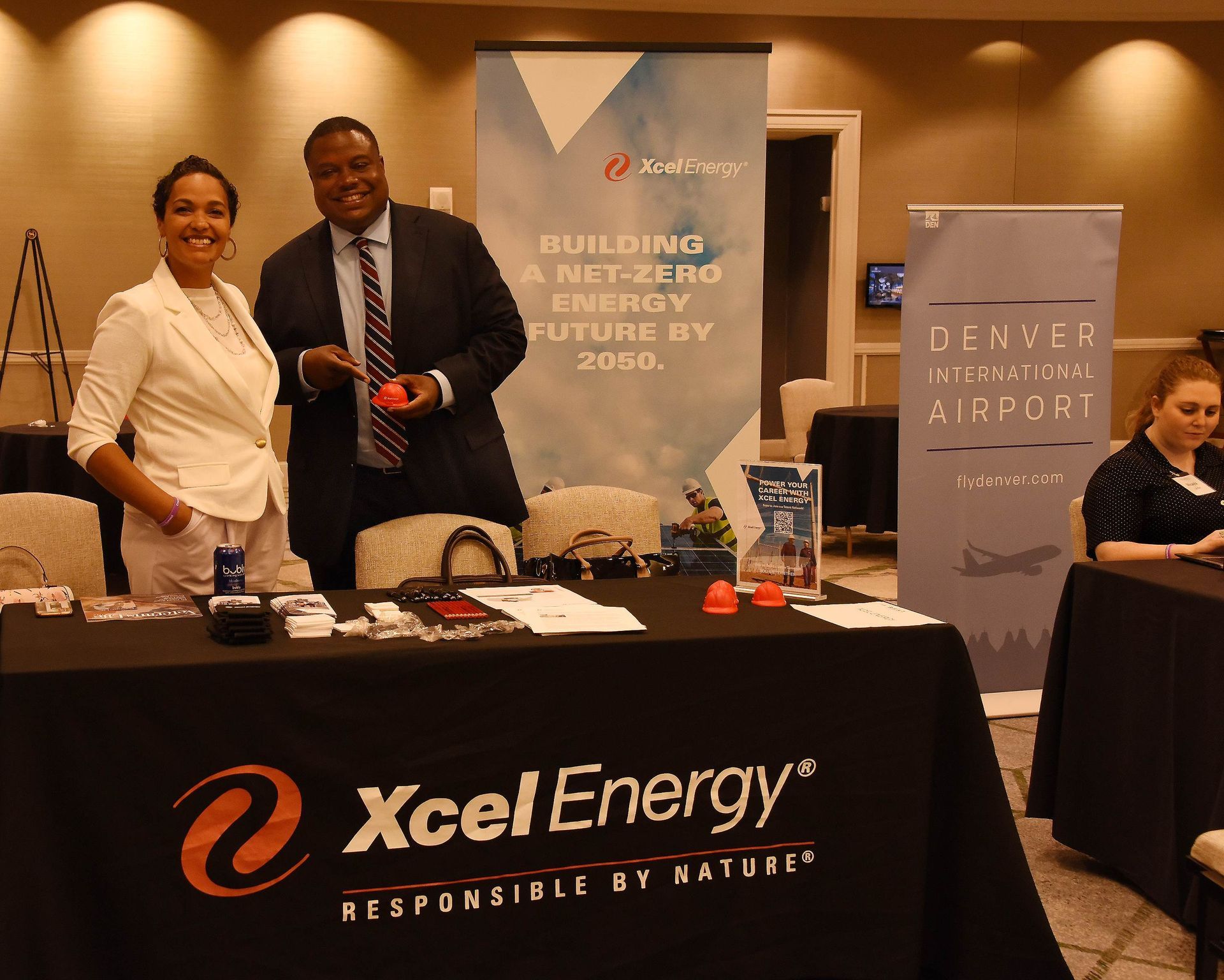 A man and woman are standing at a table with a xcel energy sign on it