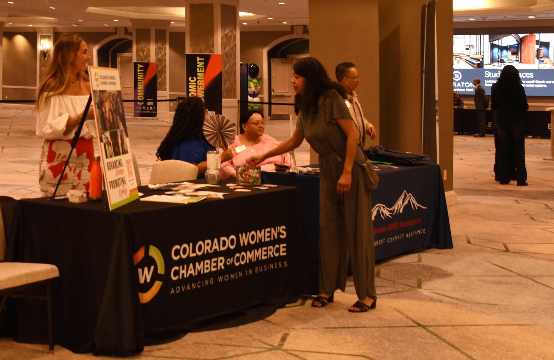 A woman is standing in front of a table that says colorado women 's chamber of commerce