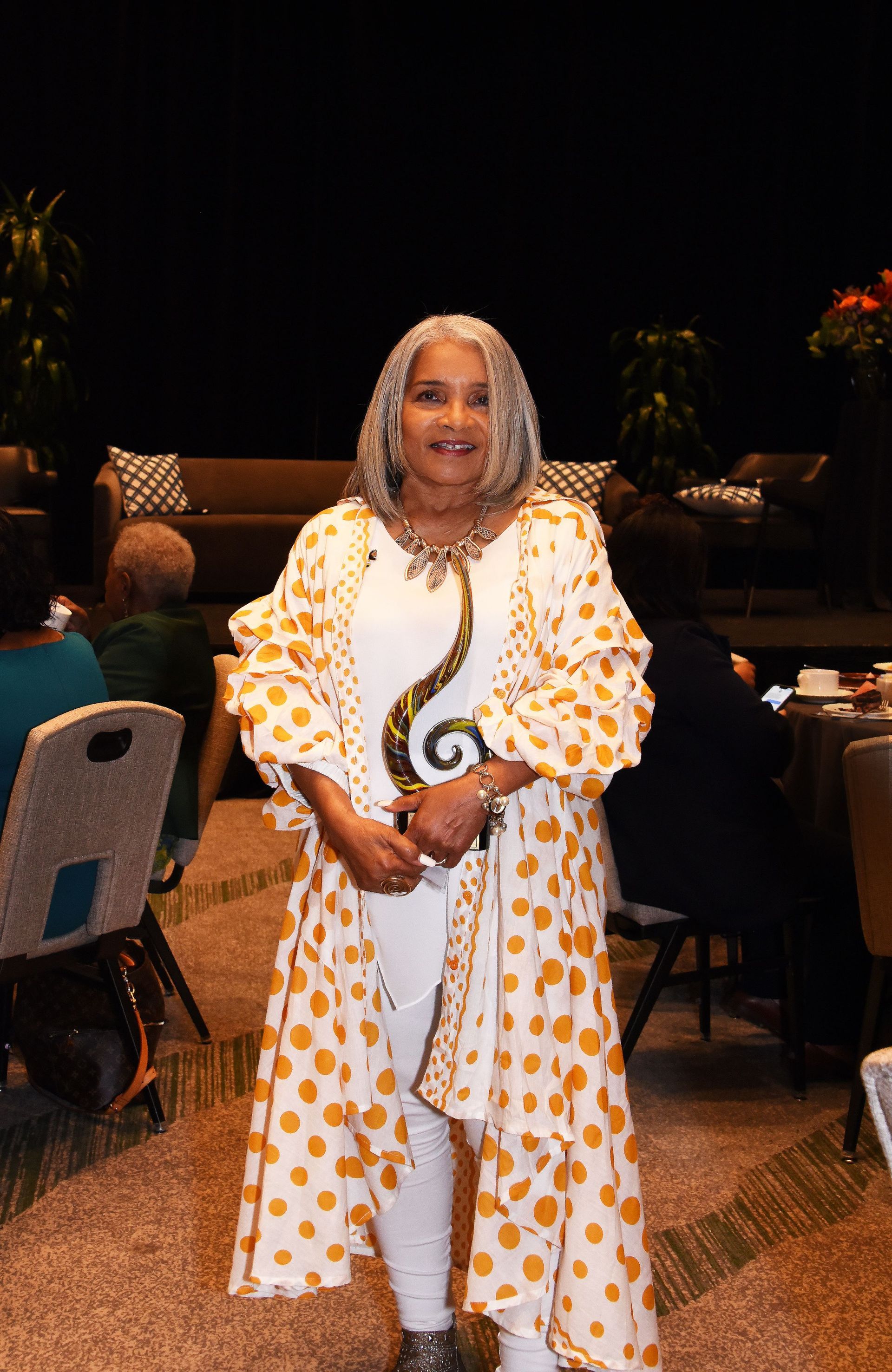 A woman is standing in a room wearing a yellow and white polka dot dress.