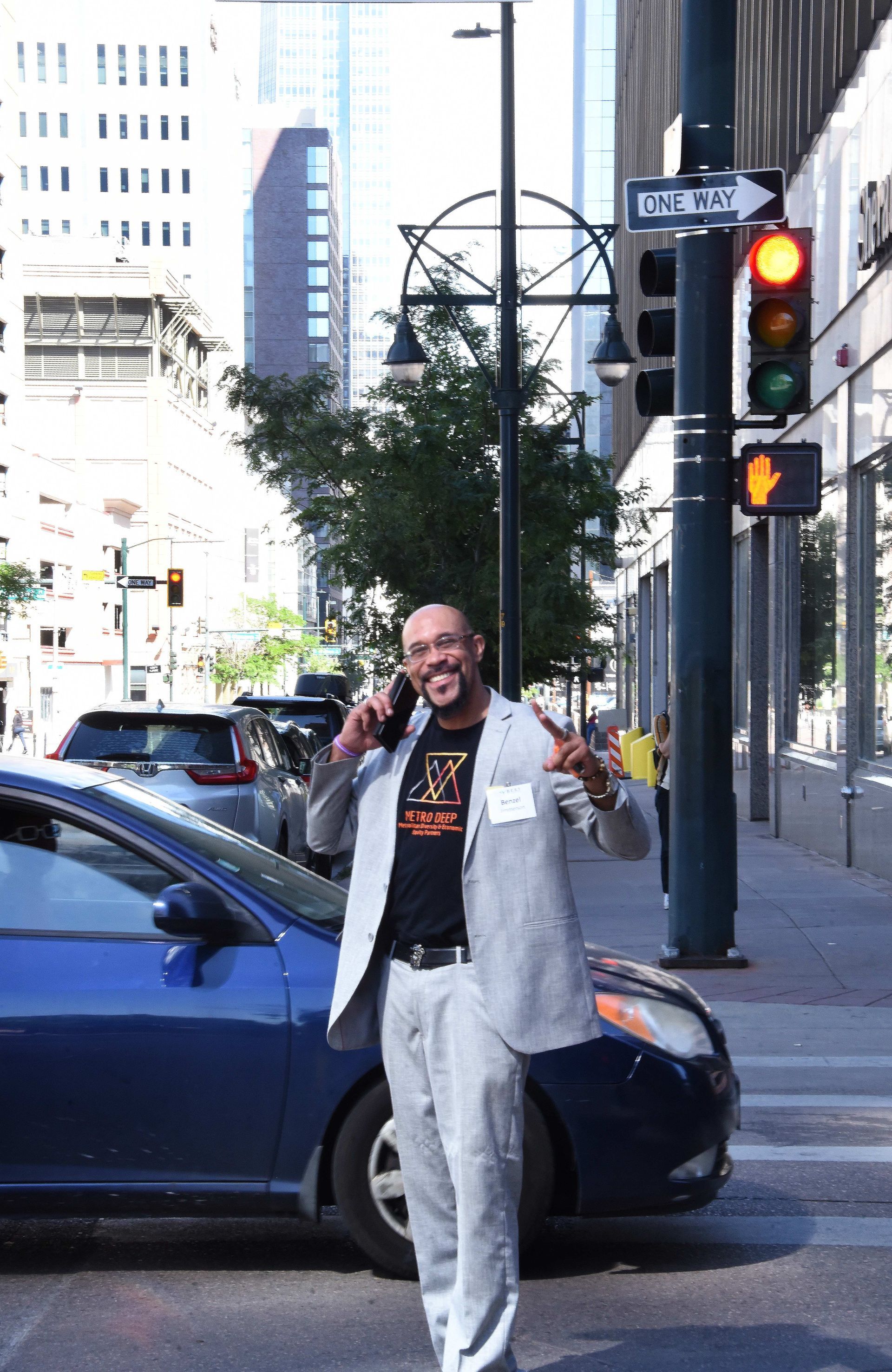A man in a suit is talking on a cell phone in front of a blue car.