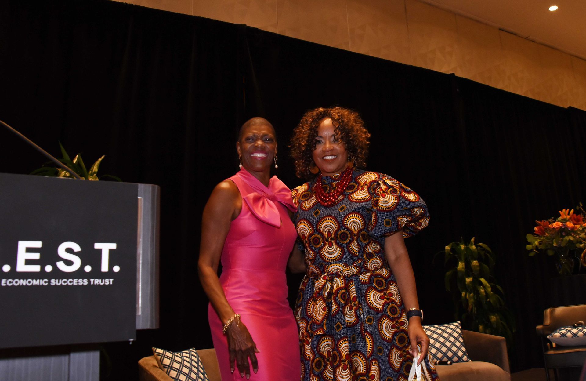 Two women are posing for a picture in front of a podium that says e.s.t.