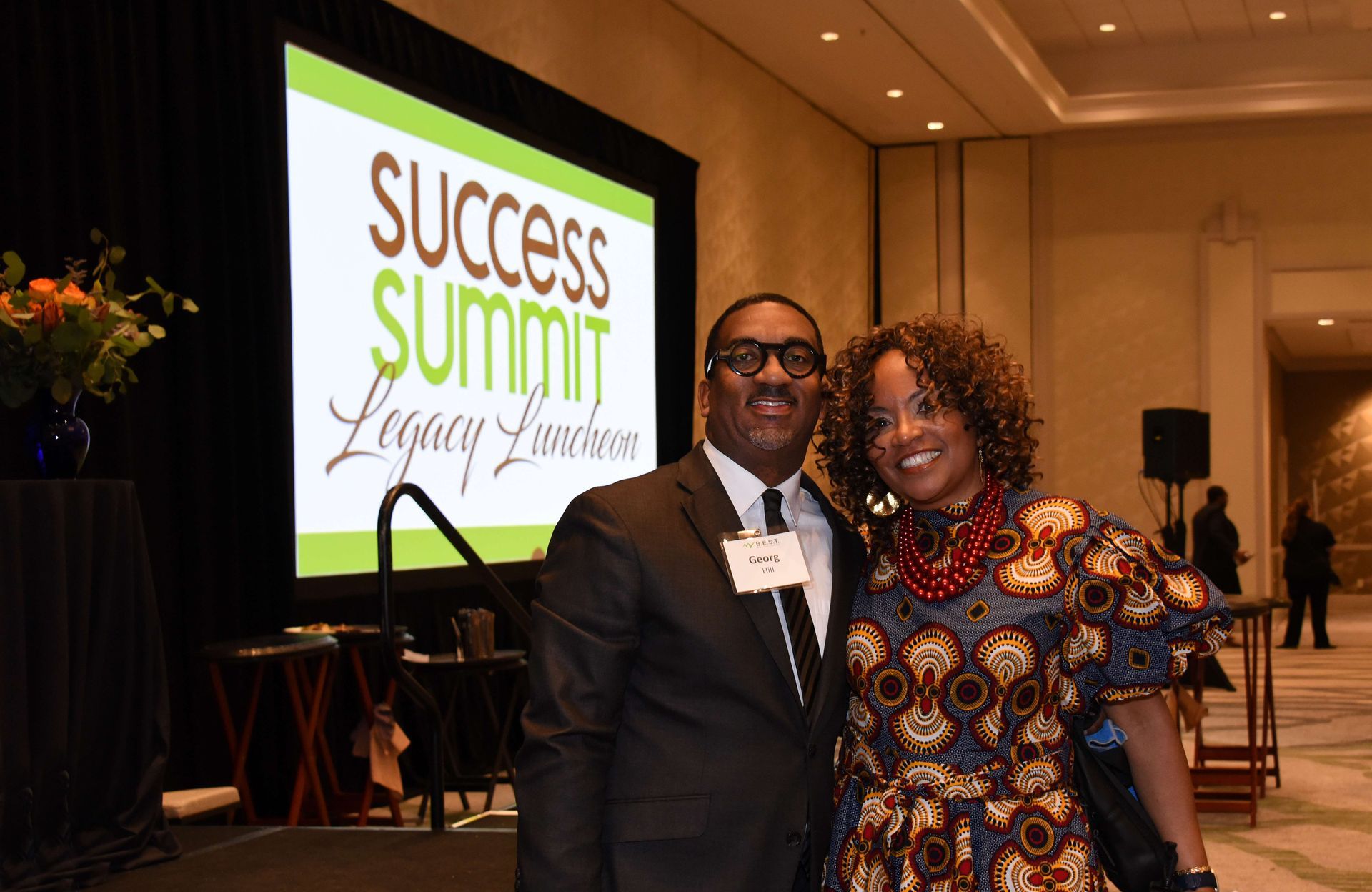 A man and a woman are posing for a picture in front of a success summit sign.