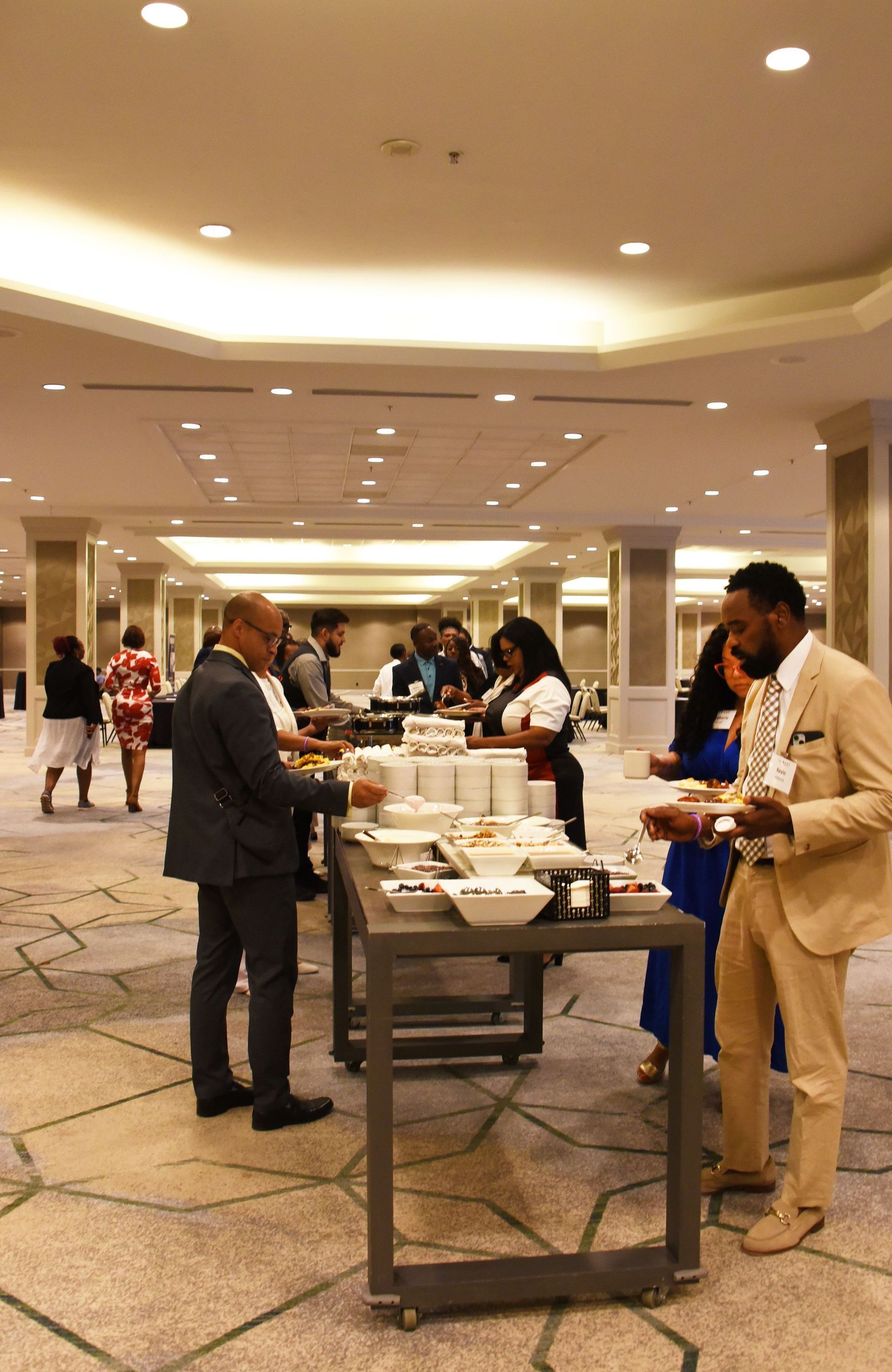 A group of people are standing around a buffet table in a large room.