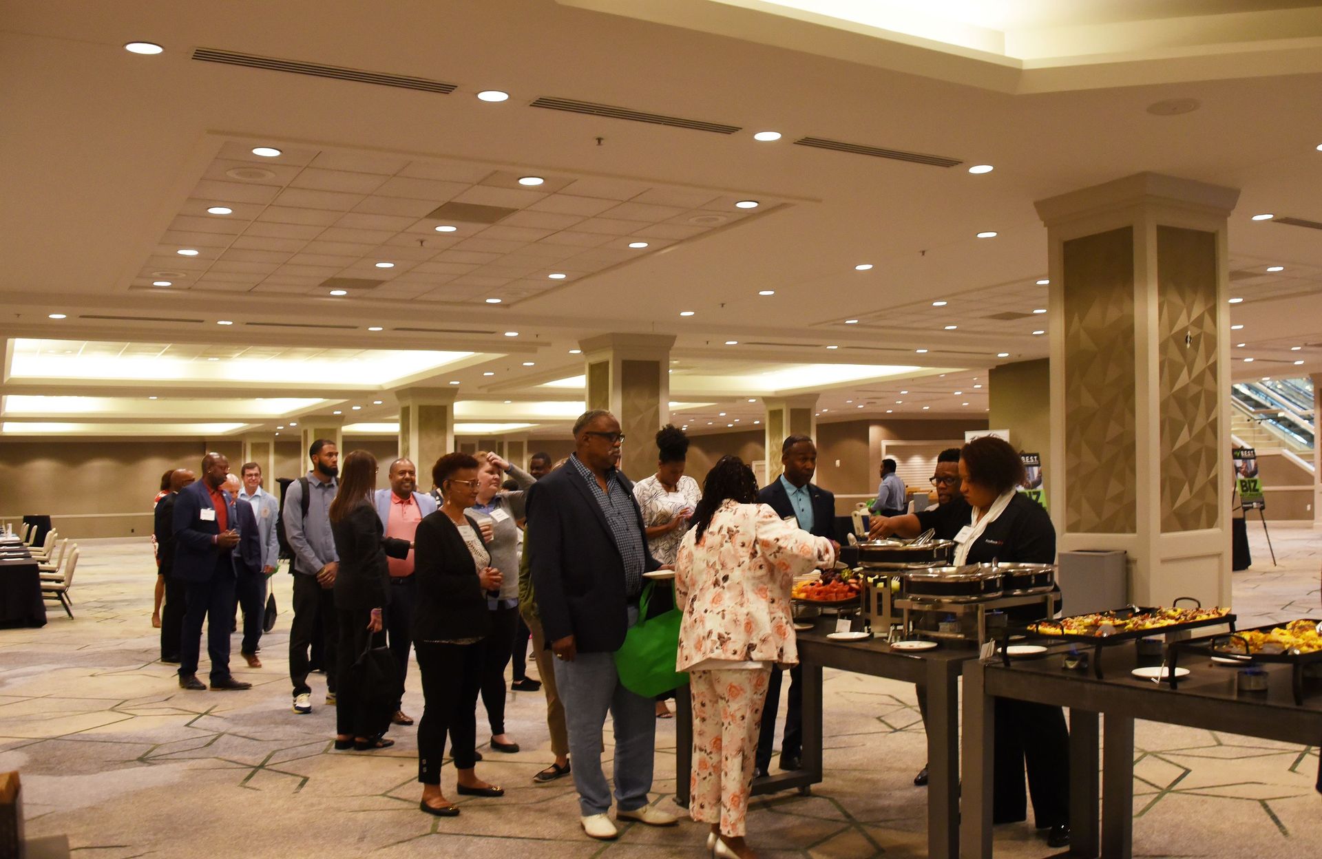 A group of people are standing around a buffet table in a large room.
