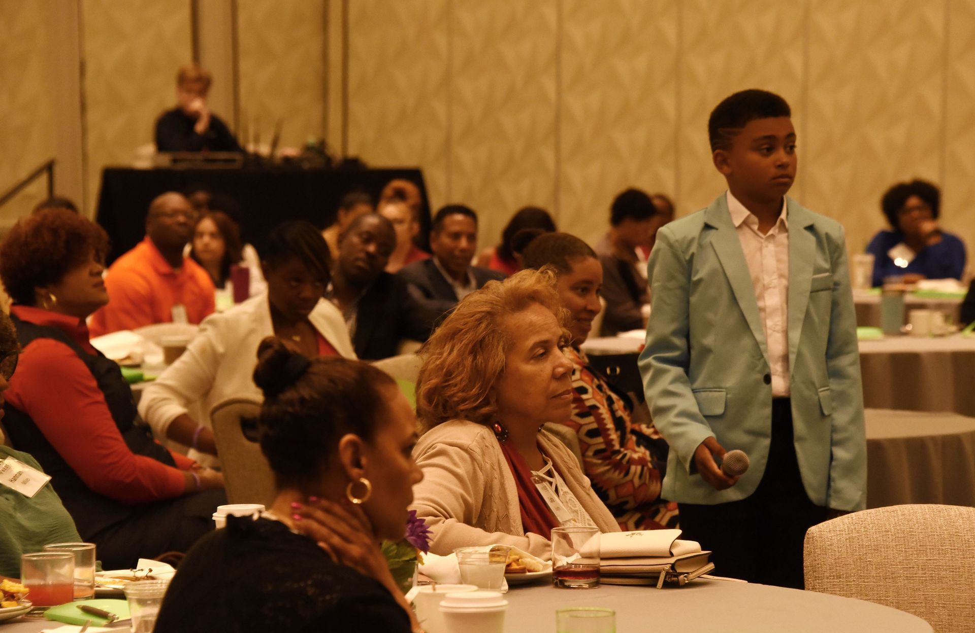 A boy in a green jacket is standing in front of a crowd of people