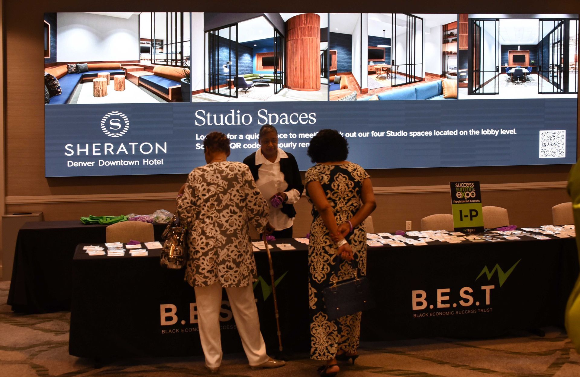 A group of people are standing around a table in front of a sign that says studio spaces.