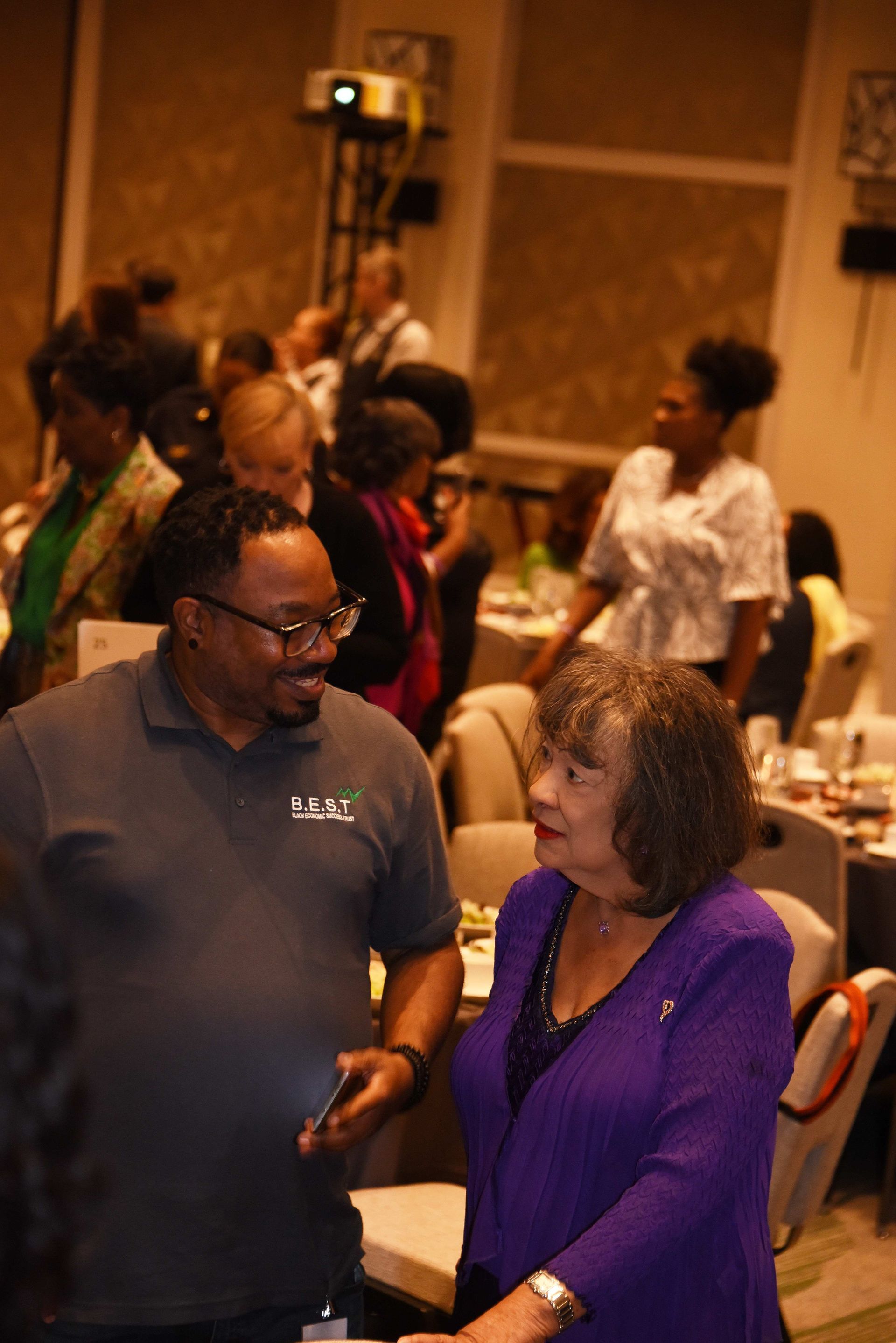 A woman in a purple jacket is talking to a man in a grey shirt.