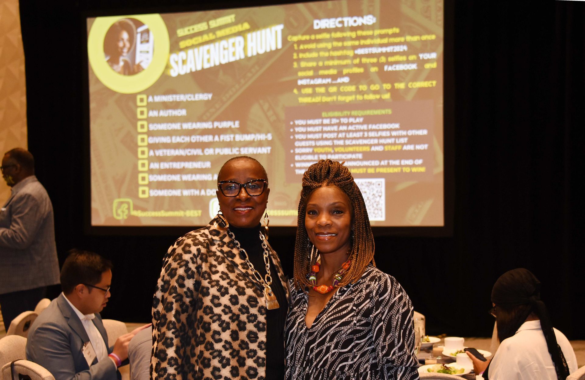 Two women are posing for a picture in front of a screen that says scavenger hunt.