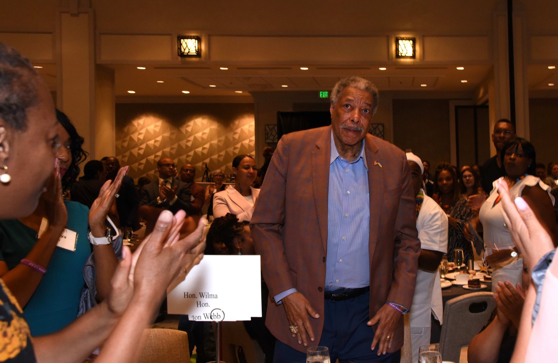 A man in a suit is standing in front of a crowd of people applauding.