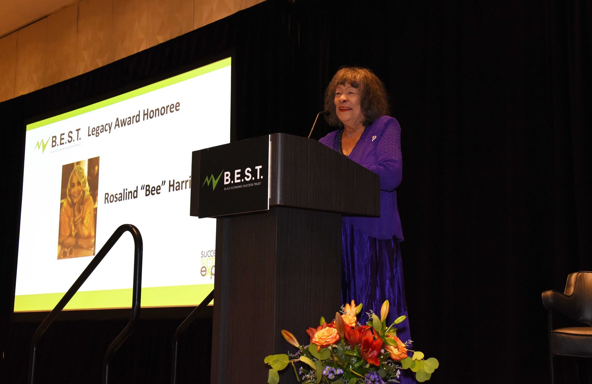 A woman in a purple dress is standing at a podium giving a speech.