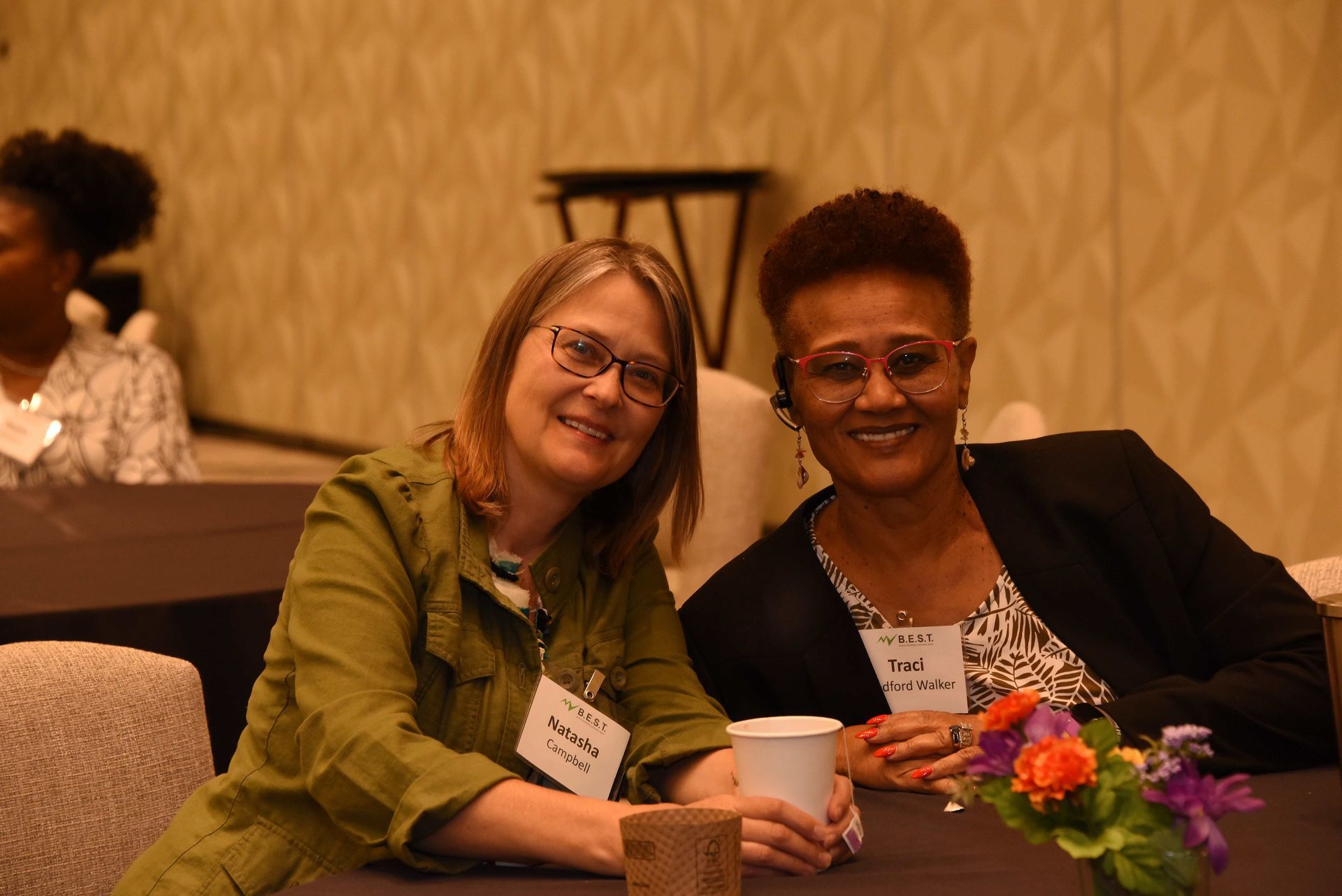 Two women are posing for a picture while sitting at a table.