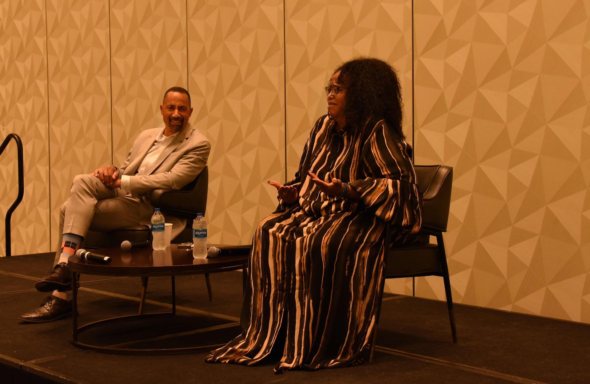 A man and a woman are sitting at a table on a stage.