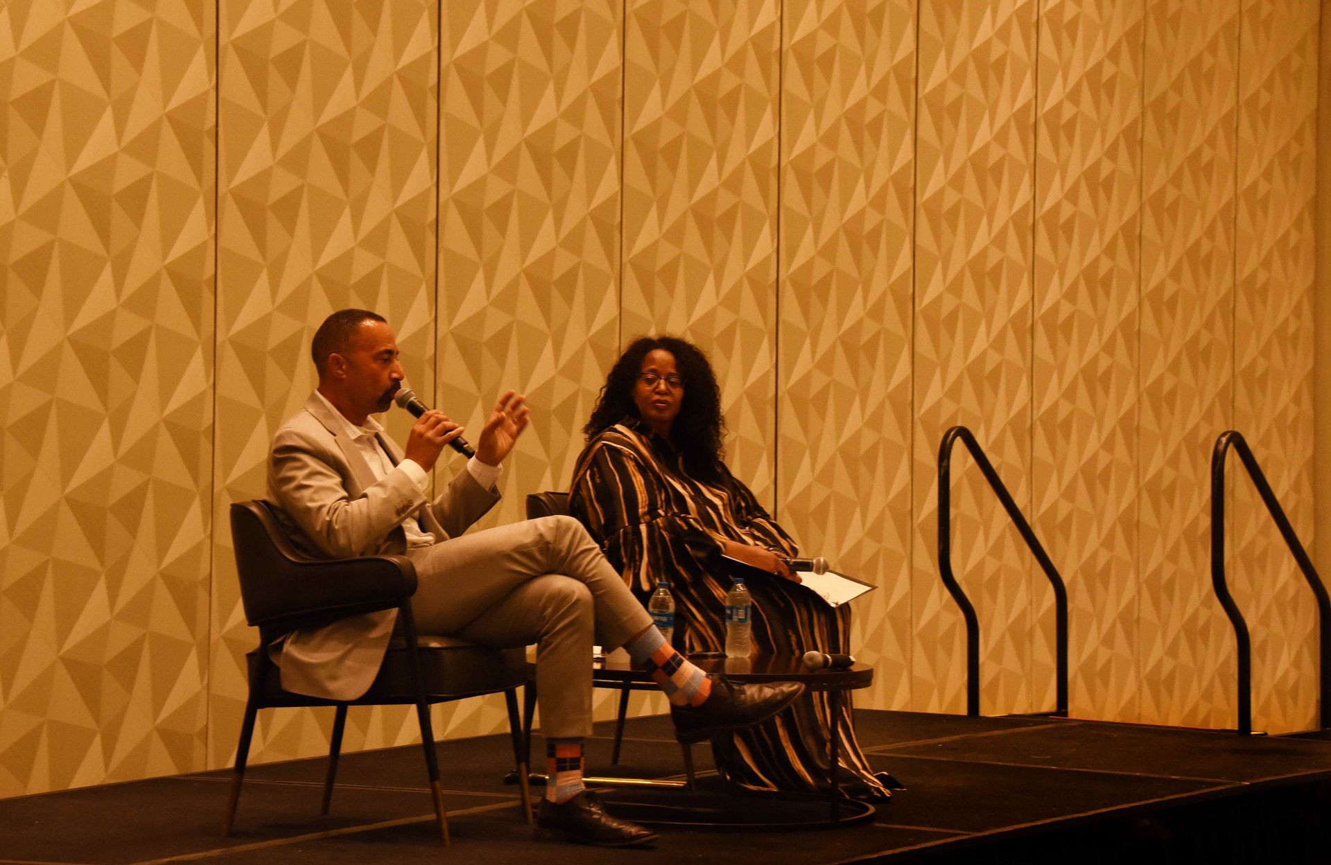 A man and a woman are sitting on a stage talking to each other.