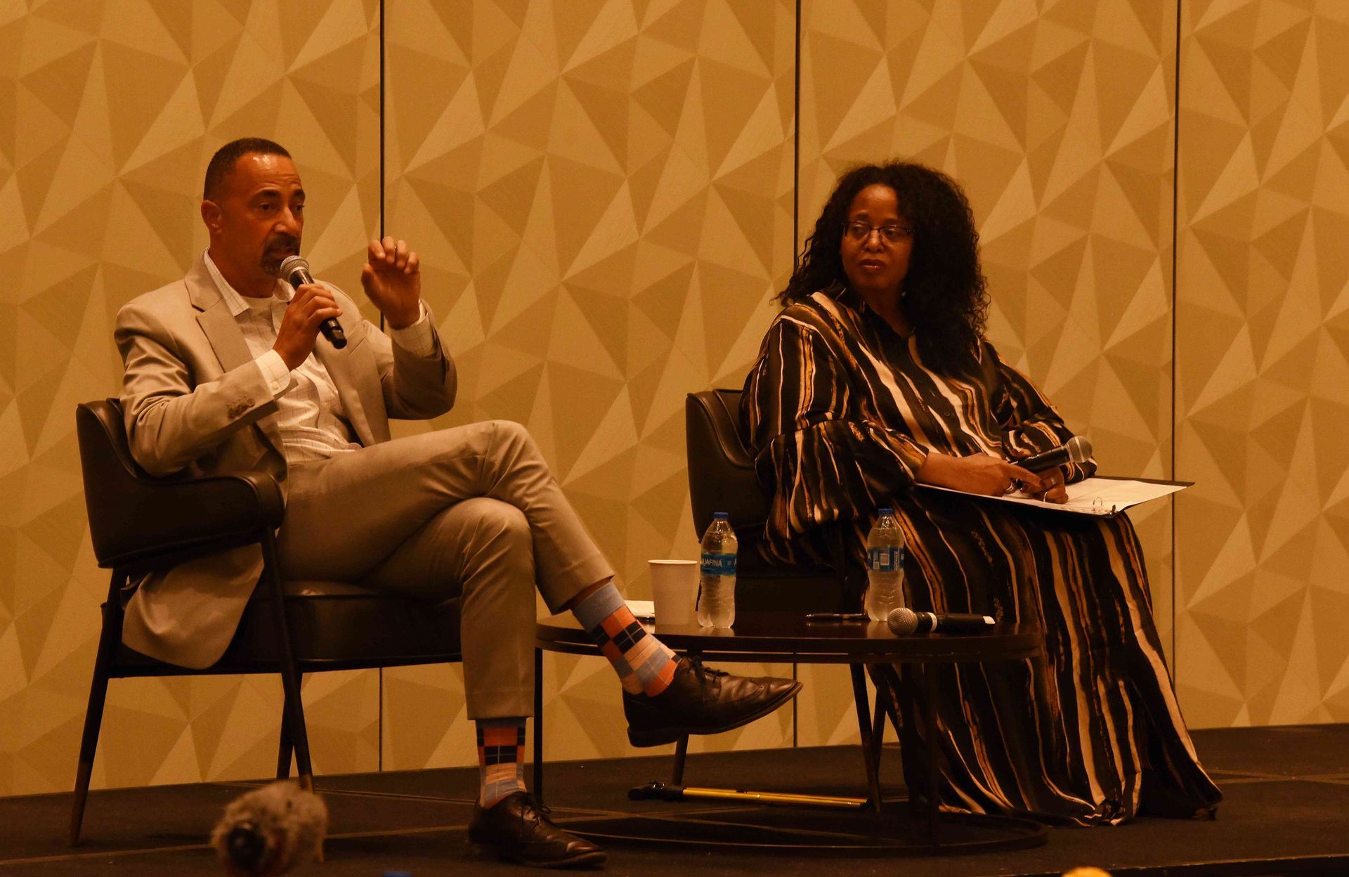 A man is sitting in a chair talking into a microphone while a woman sits in a chair.