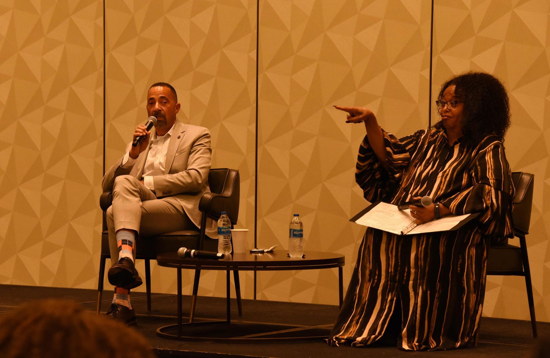 A man and a woman are sitting on a stage talking to each other.