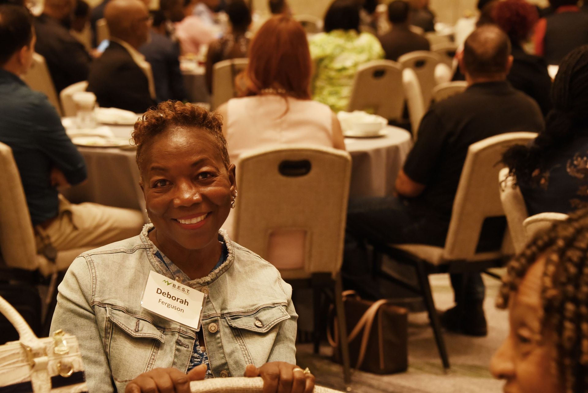 A woman is smiling while sitting at a table at a conference.