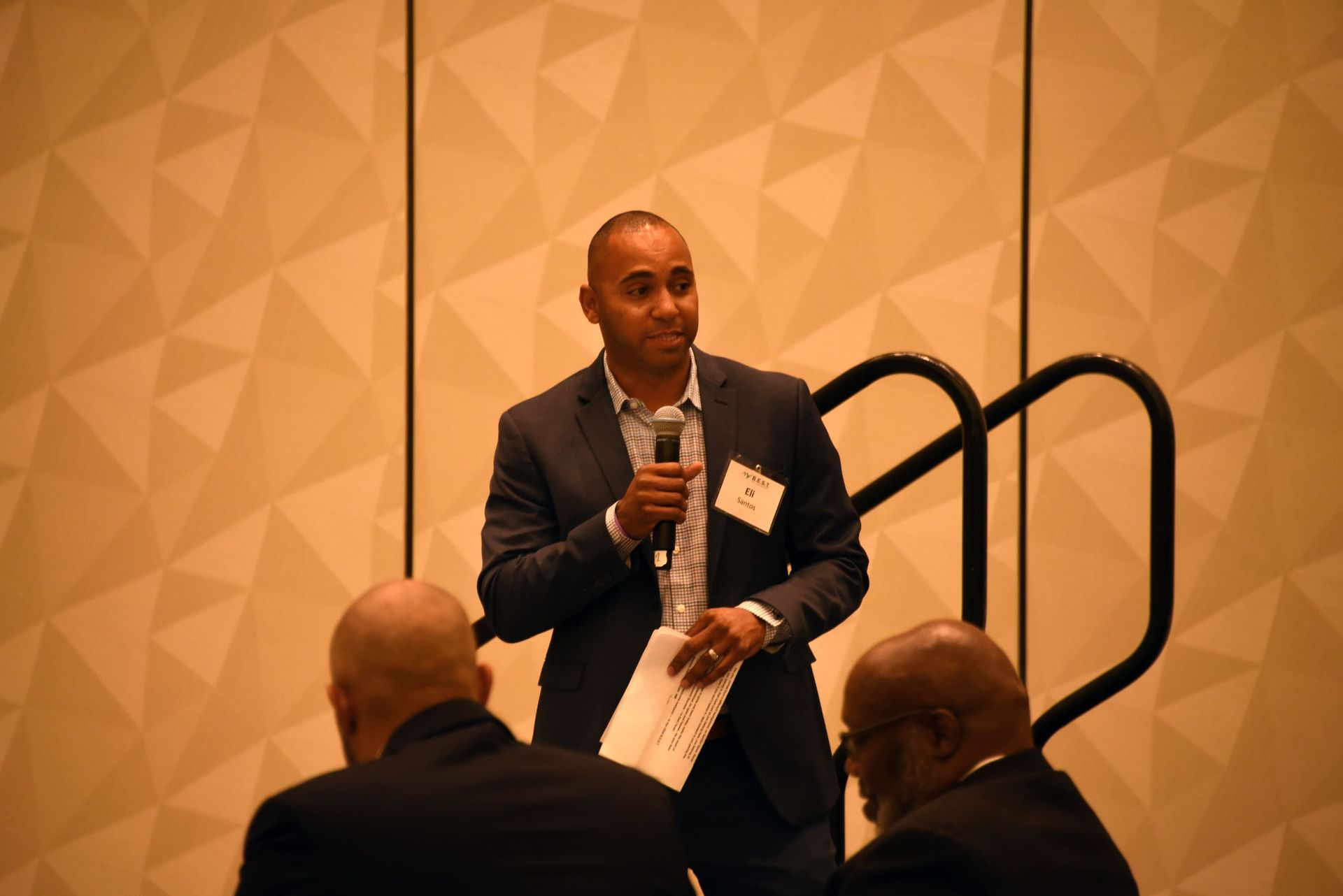 A man in a suit is holding a microphone and talking to a group of people.