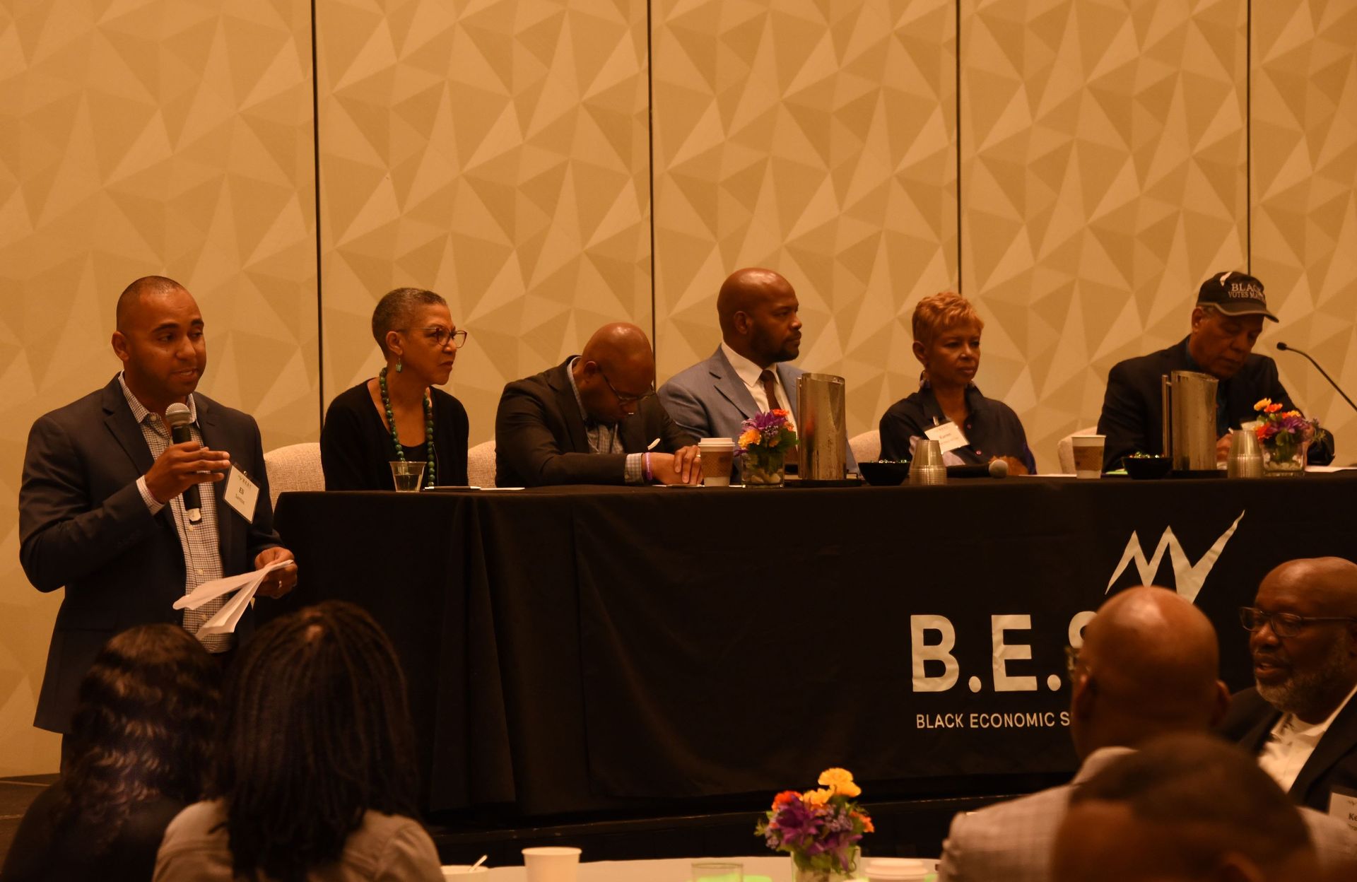 A group of people are sitting at a table with a sign that says b.e.