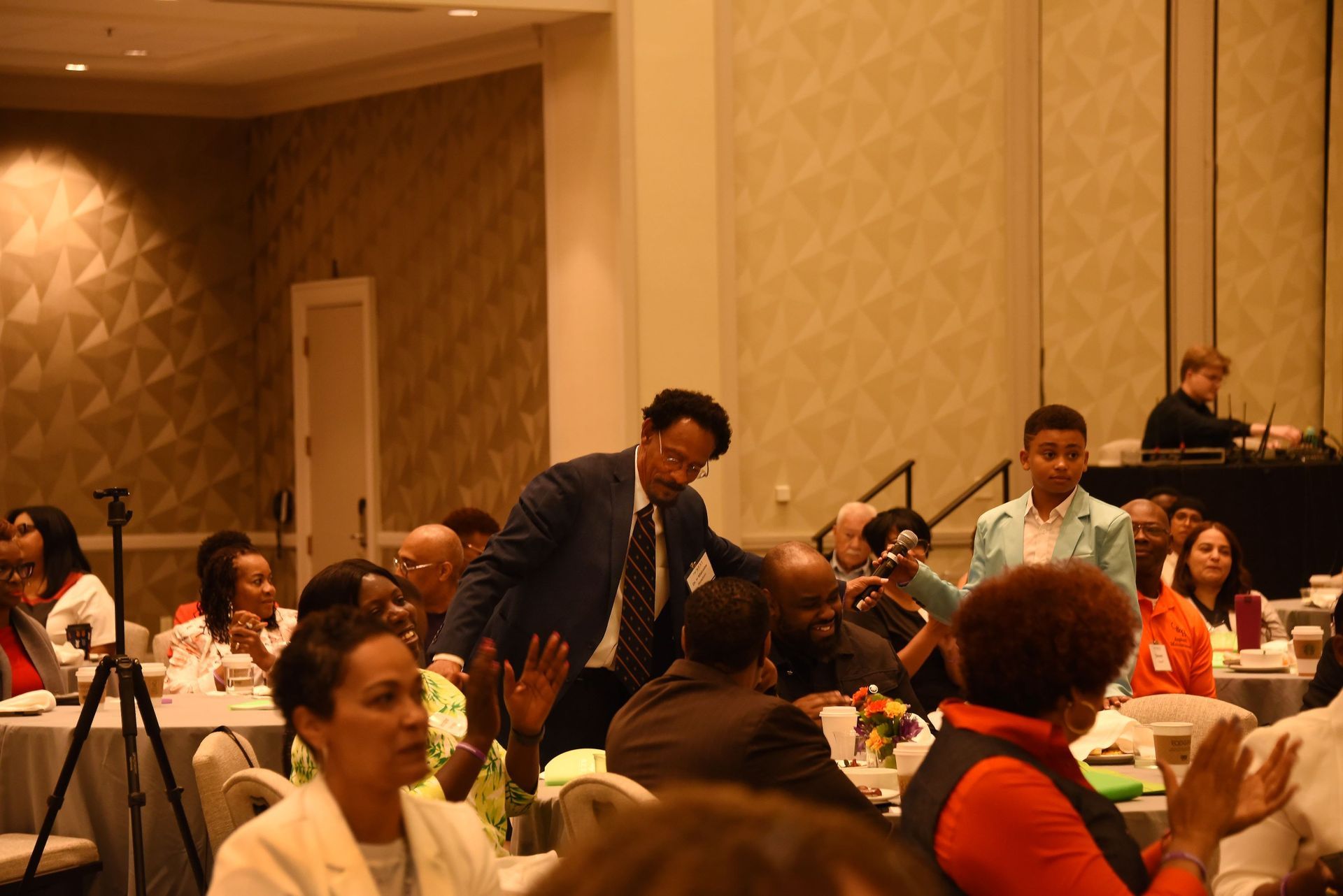 A man in a suit and tie is talking to a group of people sitting at tables.