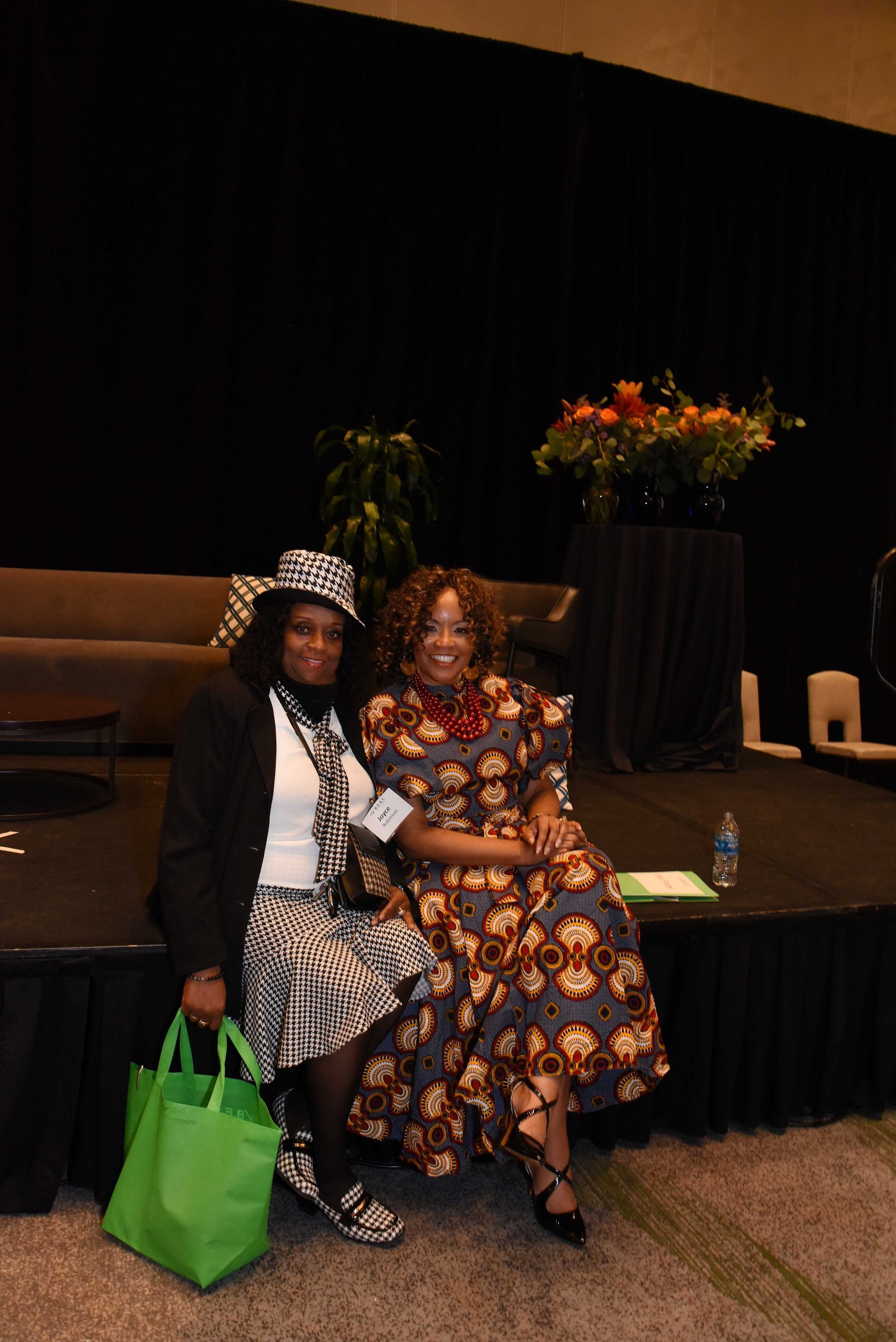 Two women are posing for a picture while sitting on a stage.
