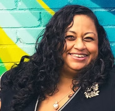 A woman with curly hair is wearing a yellow scarf and a pearl necklace