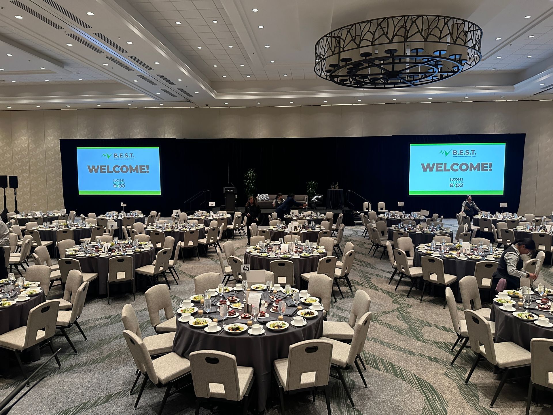 A large room filled with tables and chairs and two screens that say welcome.