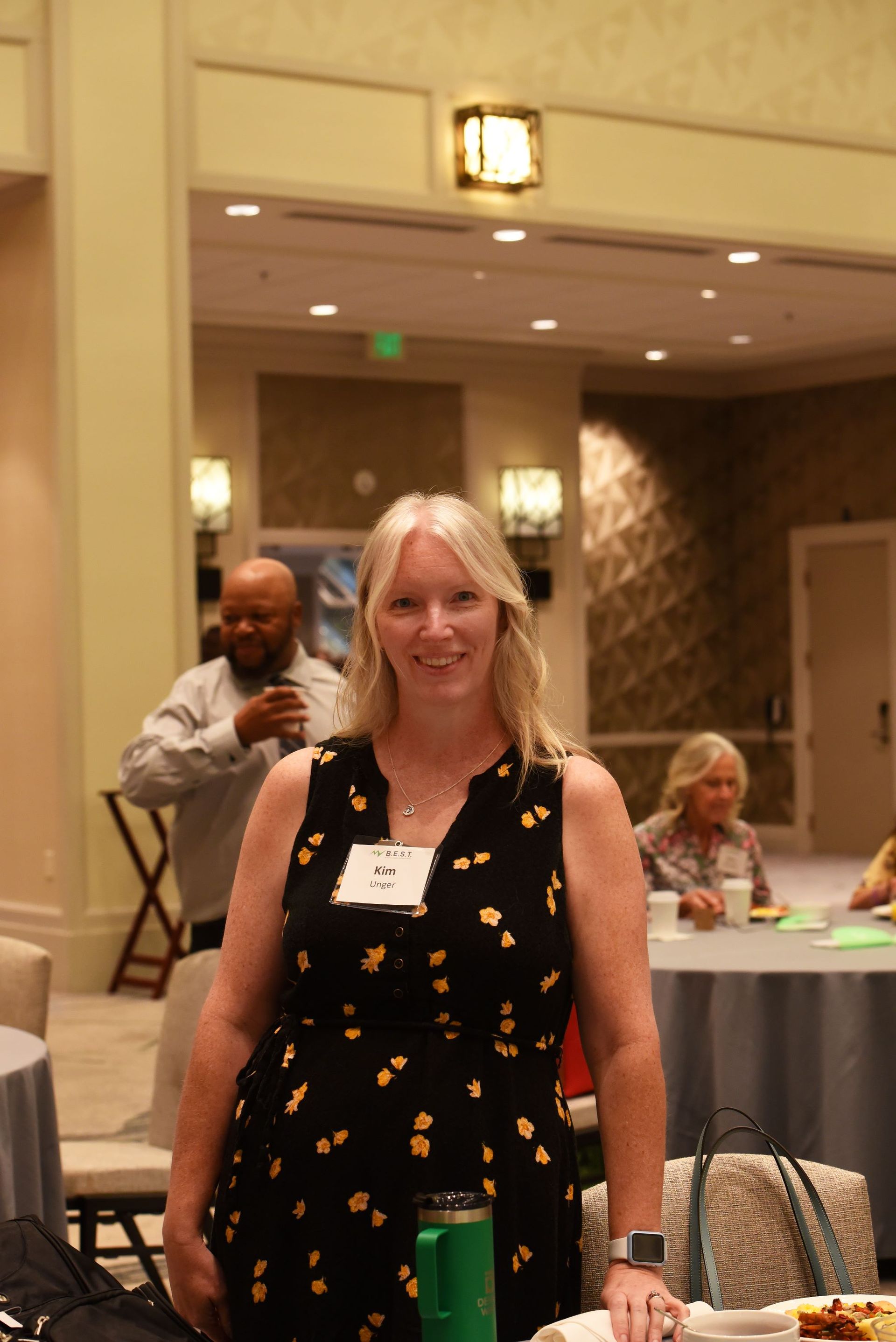 A woman in a black dress is standing in a room with tables and chairs.