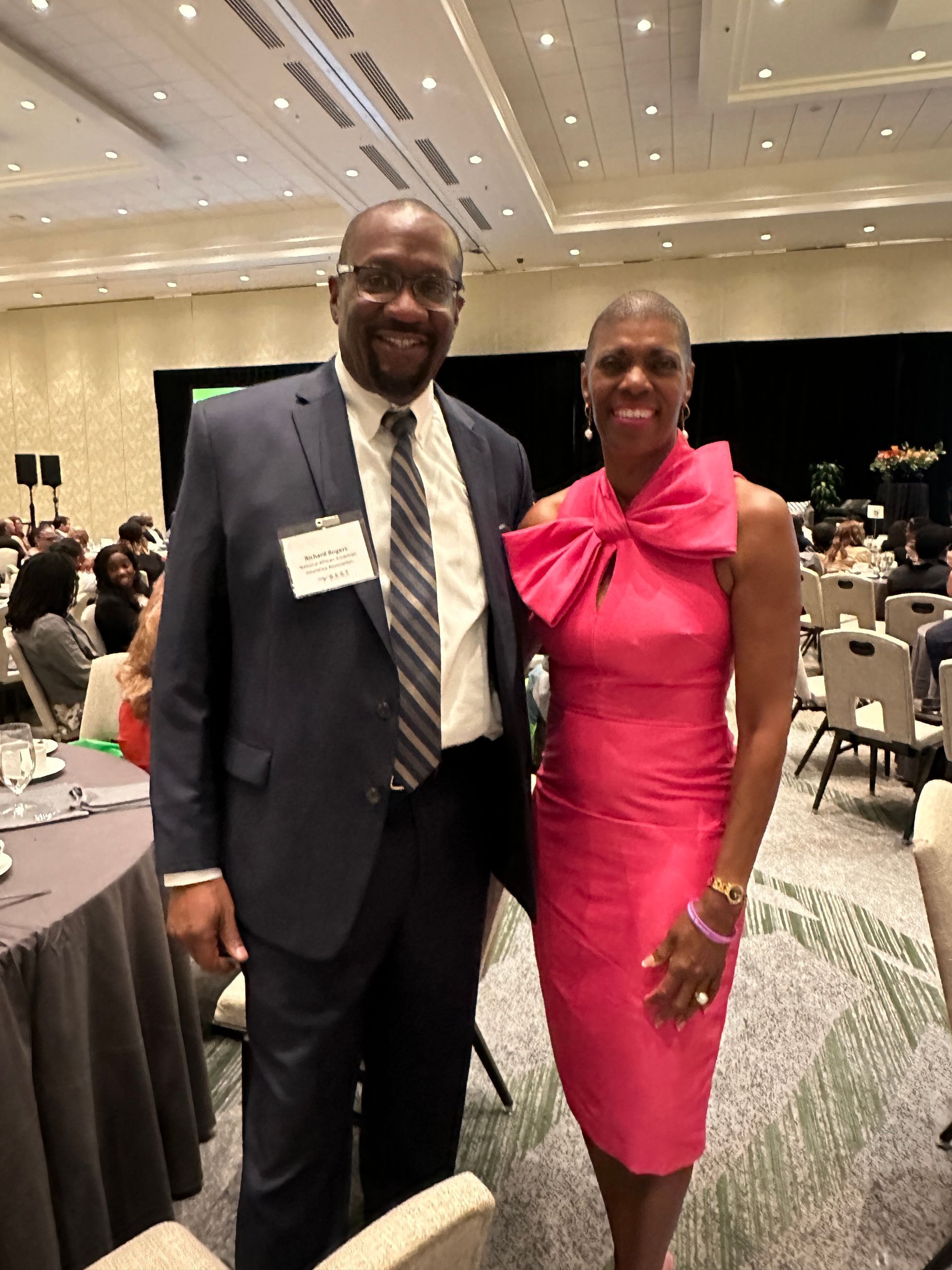 A man in a suit and tie stands next to a woman in a pink dress.