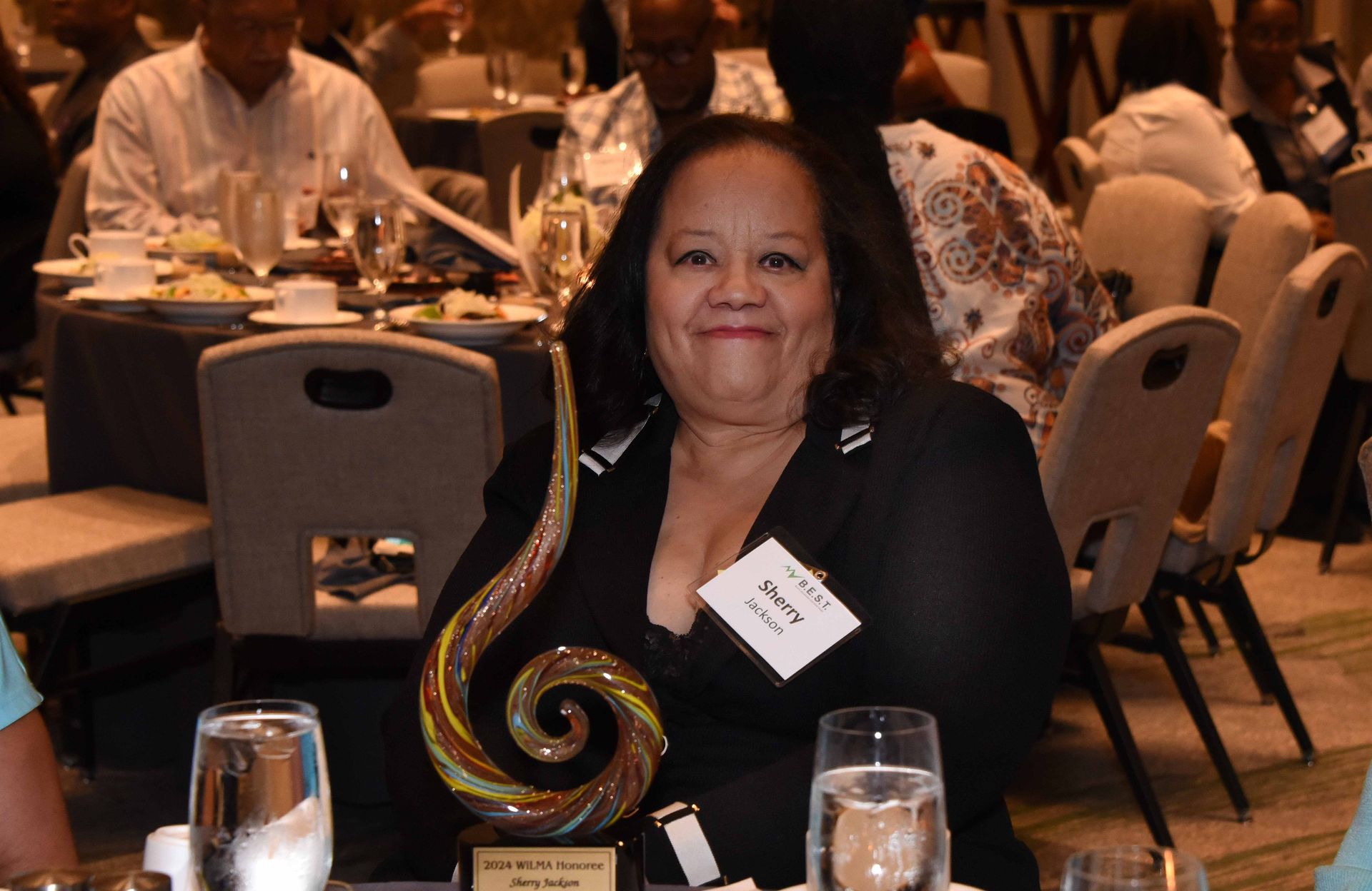 A woman is sitting at a table with a trophy in front of her.
