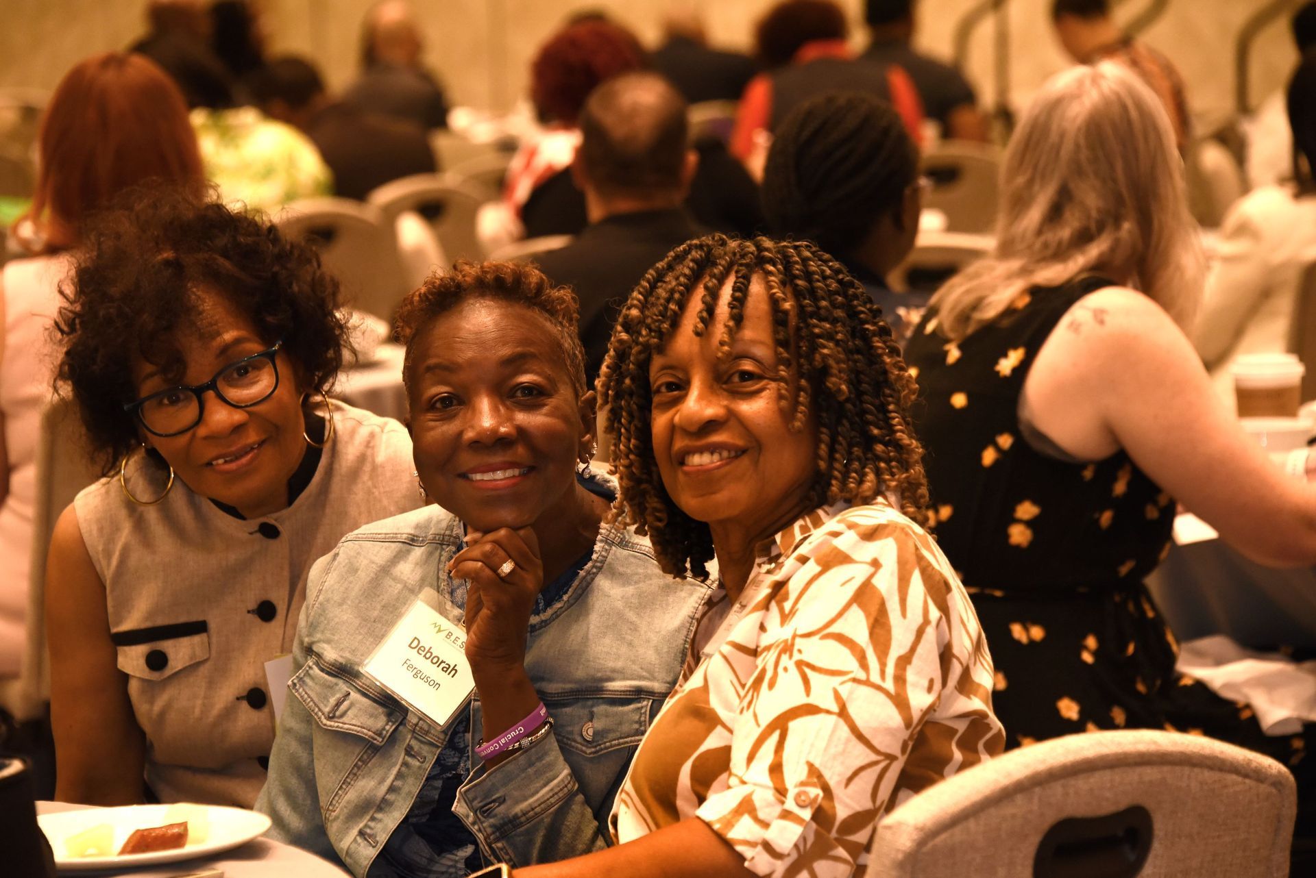 Three women are posing for a picture while sitting at a table at a conference.