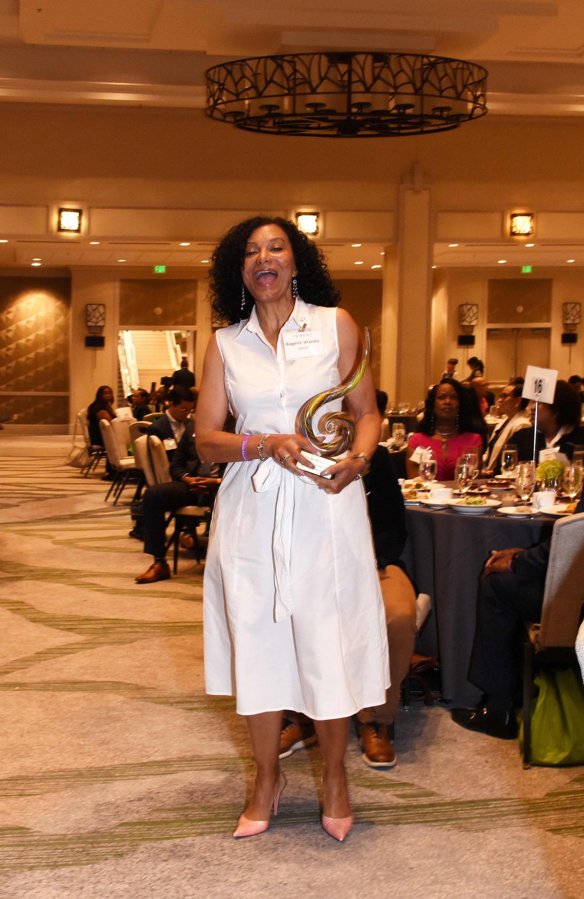 A woman in a white dress is standing in a room holding a trophy.