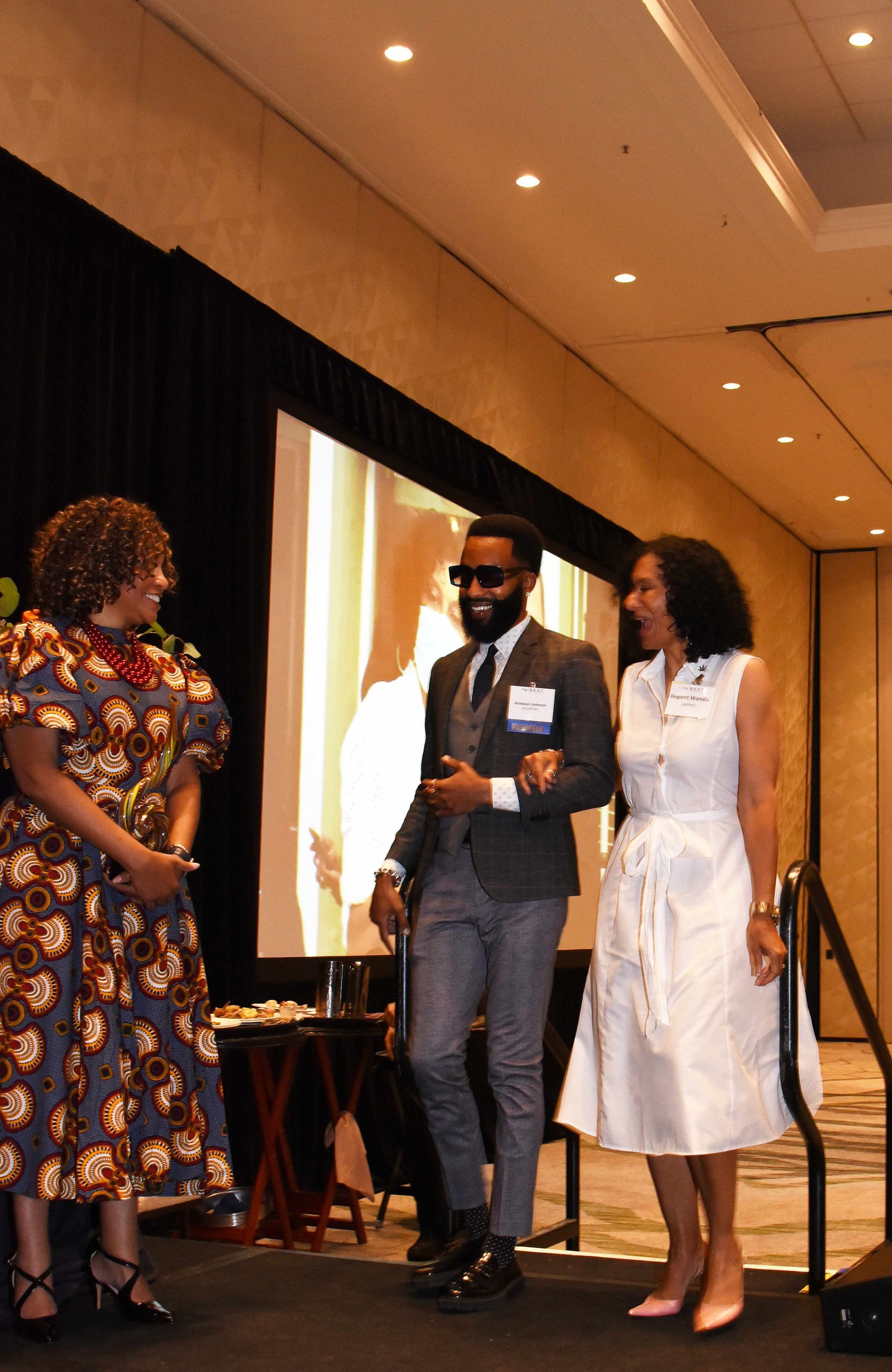 A man in a suit and tie is standing next to two women on a stage.