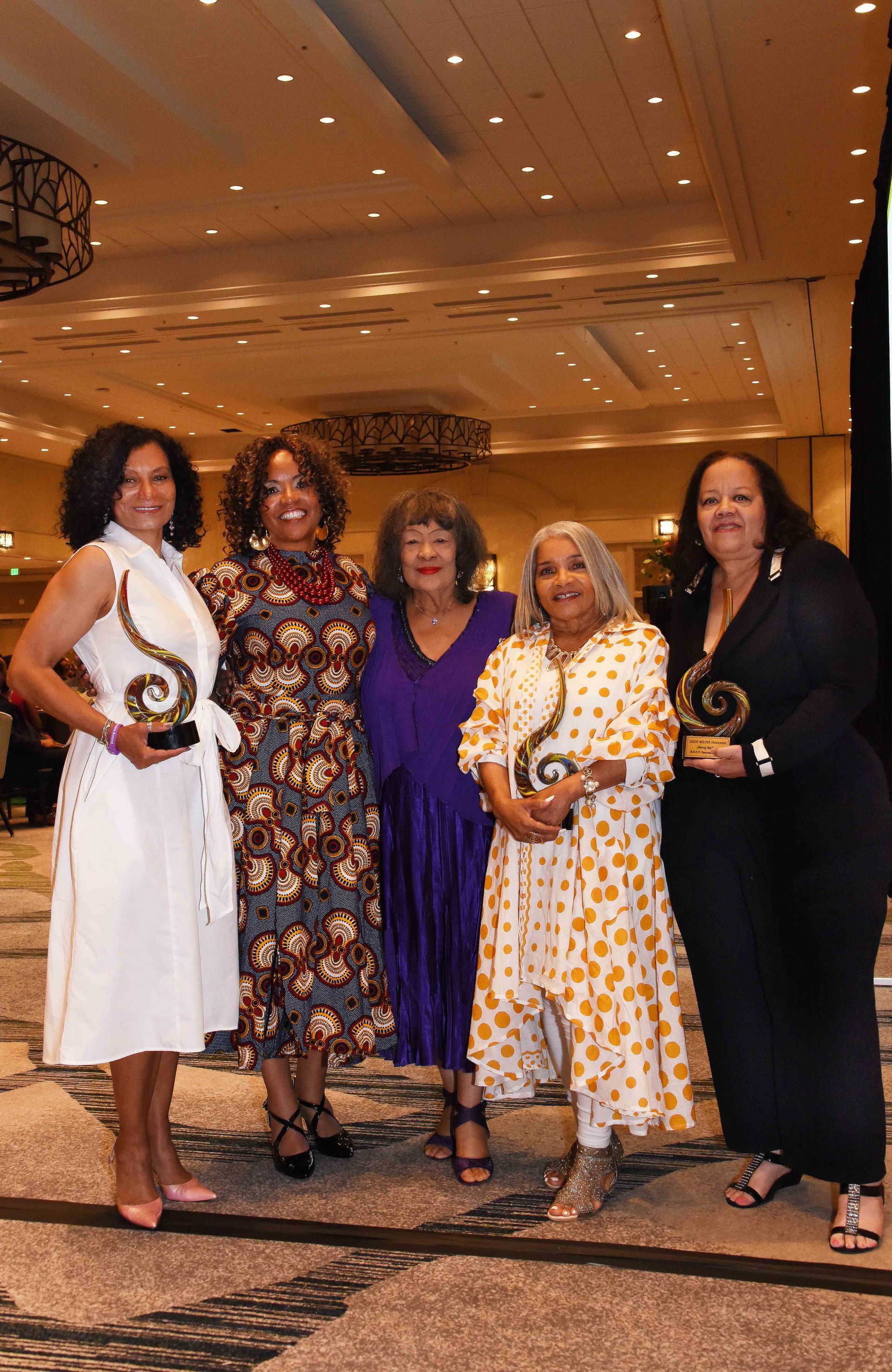 A group of women are standing next to each other in a room holding trophies.