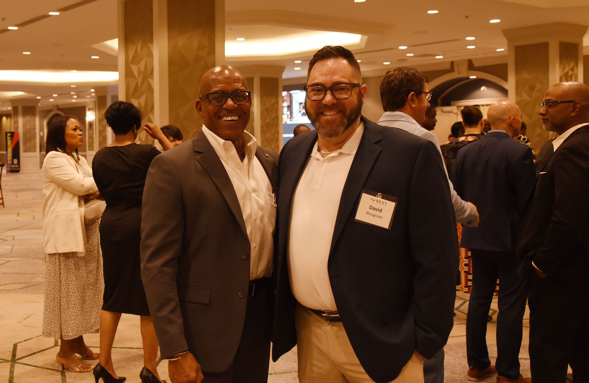 Two men in suits are posing for a picture in a hallway.