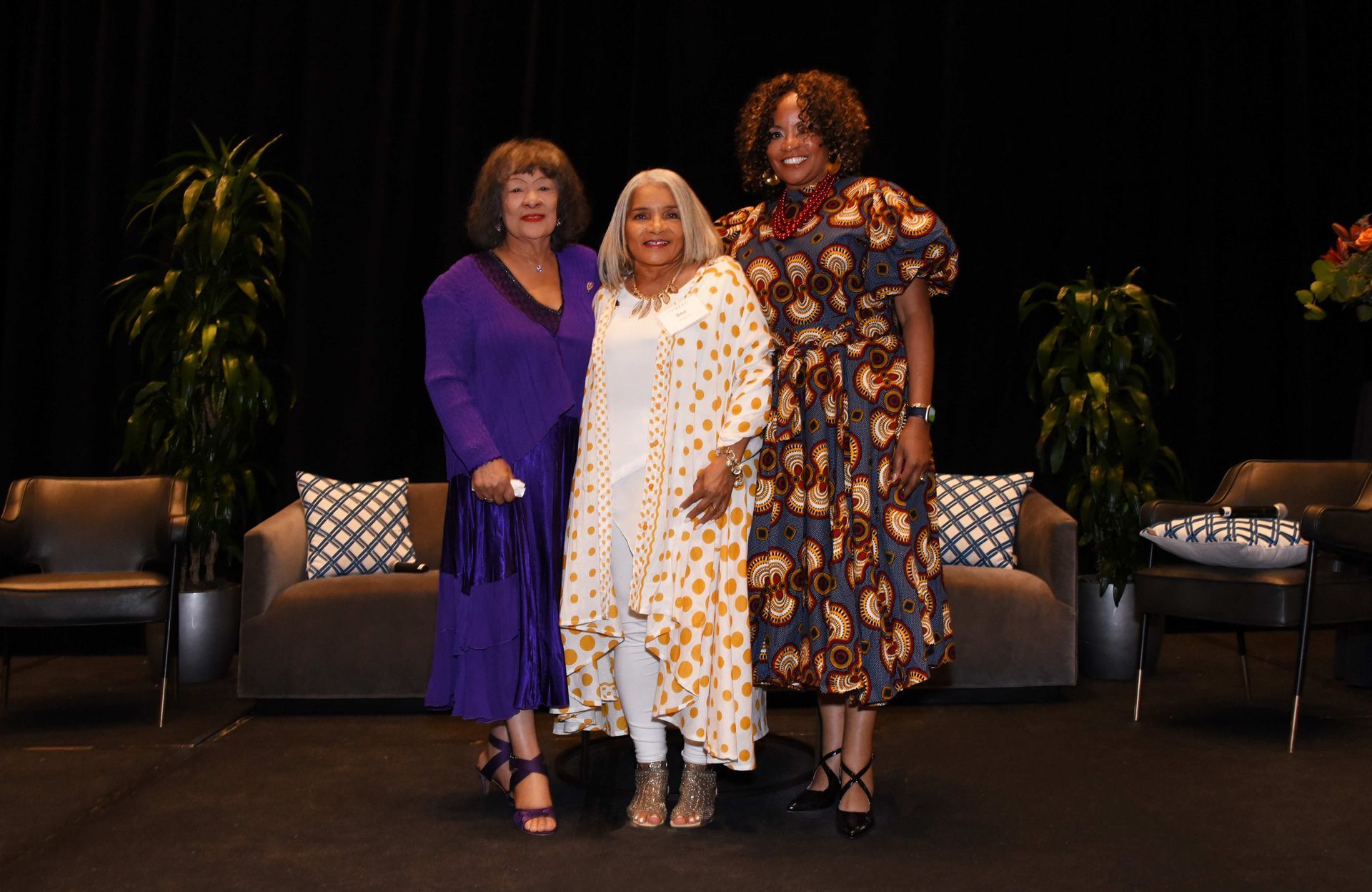 Three women are posing for a picture in front of a couch.