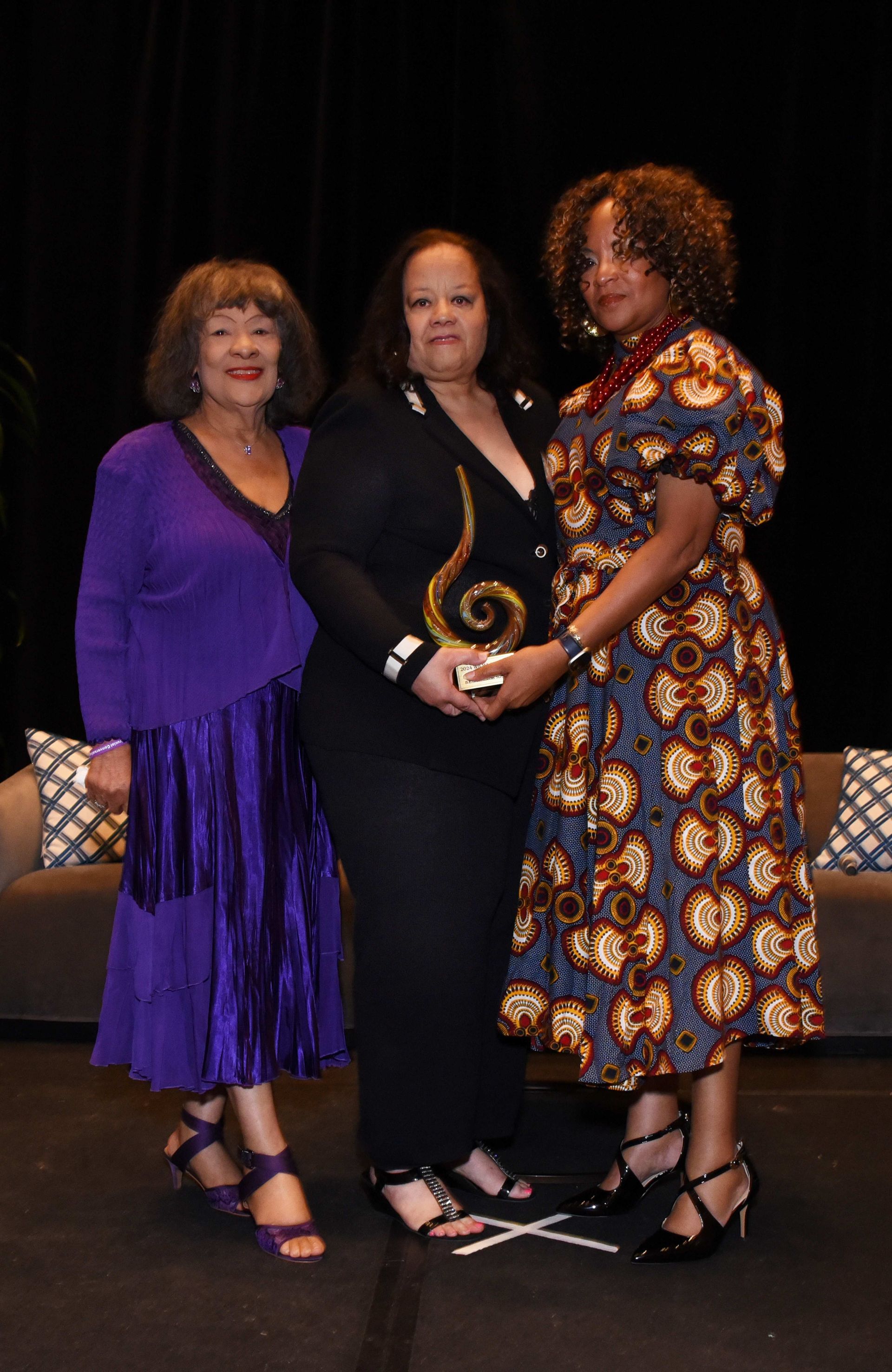 Three women are posing for a picture and one of them is holding an award