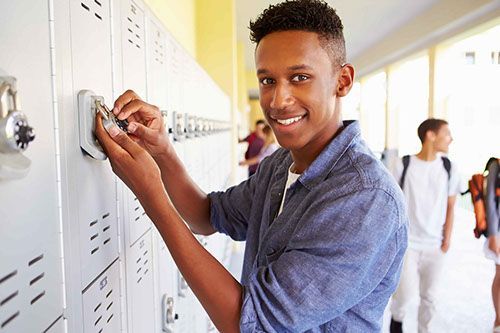 A young man is opening a locker in a school hallway.