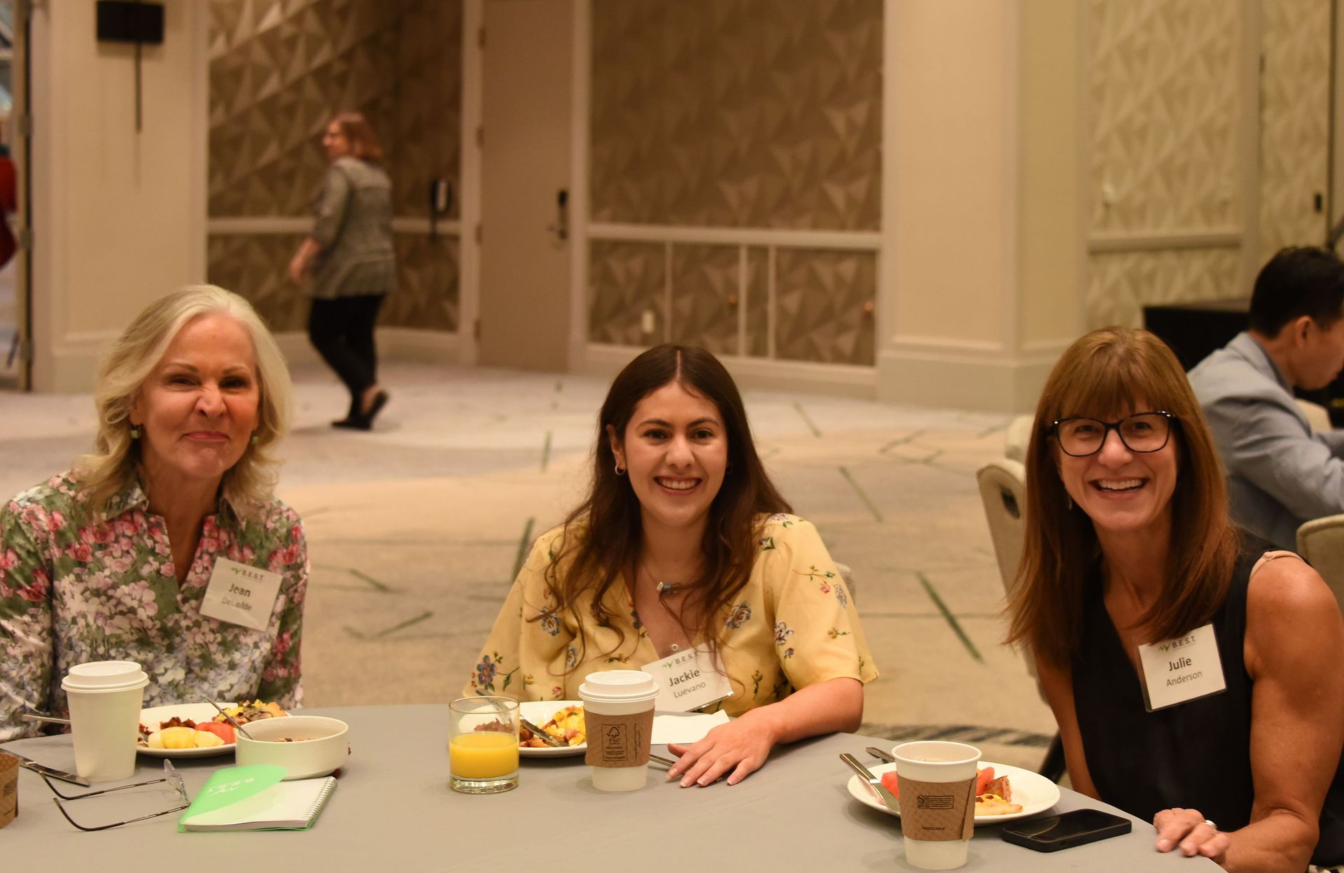 Three women are sitting at a table with plates of food and cups of coffee.