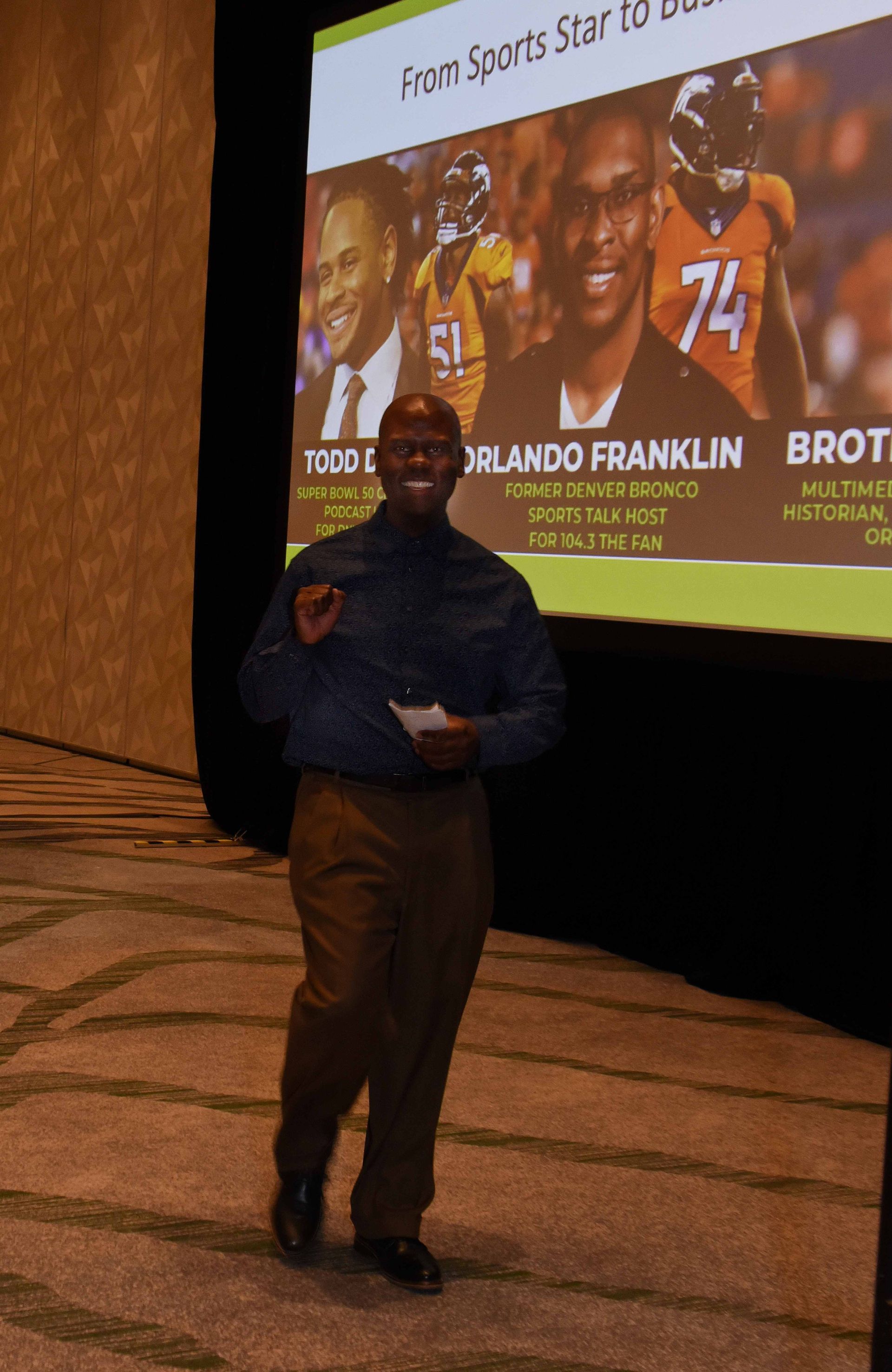 A man stands in front of a large screen that says fram sports star to business