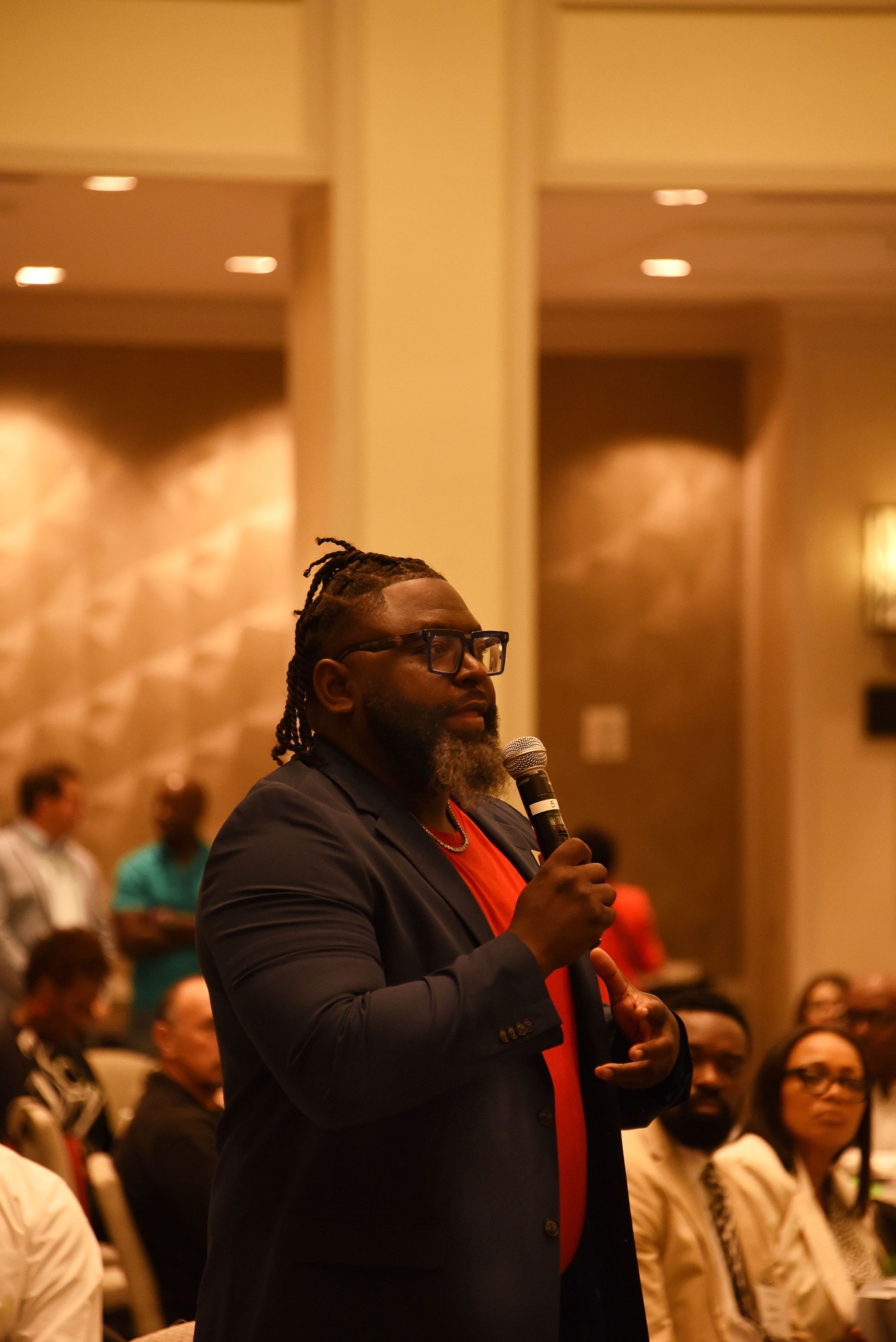 A man in a suit is holding a microphone in front of a crowd.
