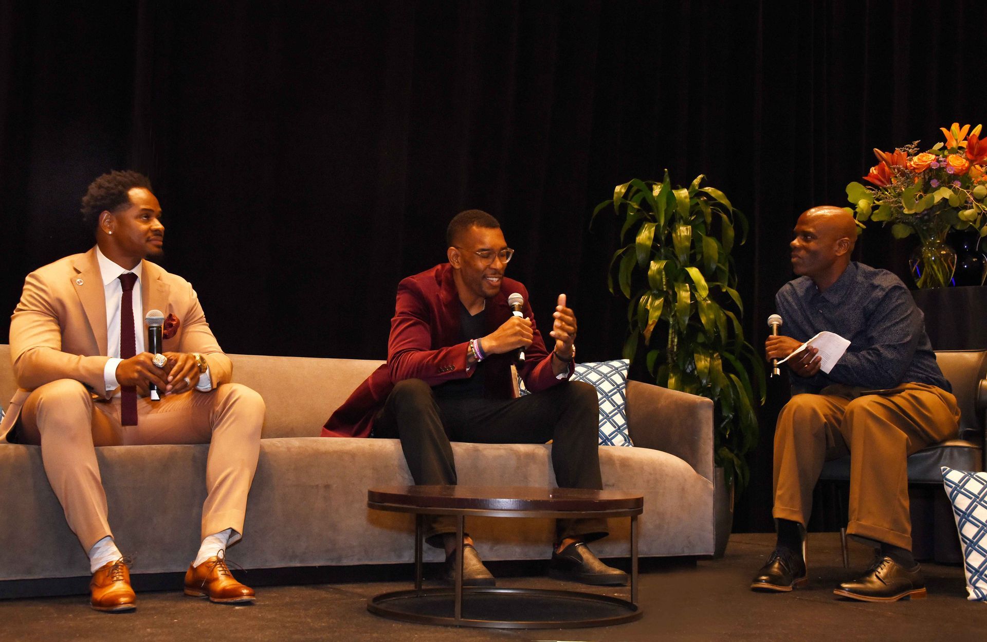 Three men are sitting on a couch talking to each other.