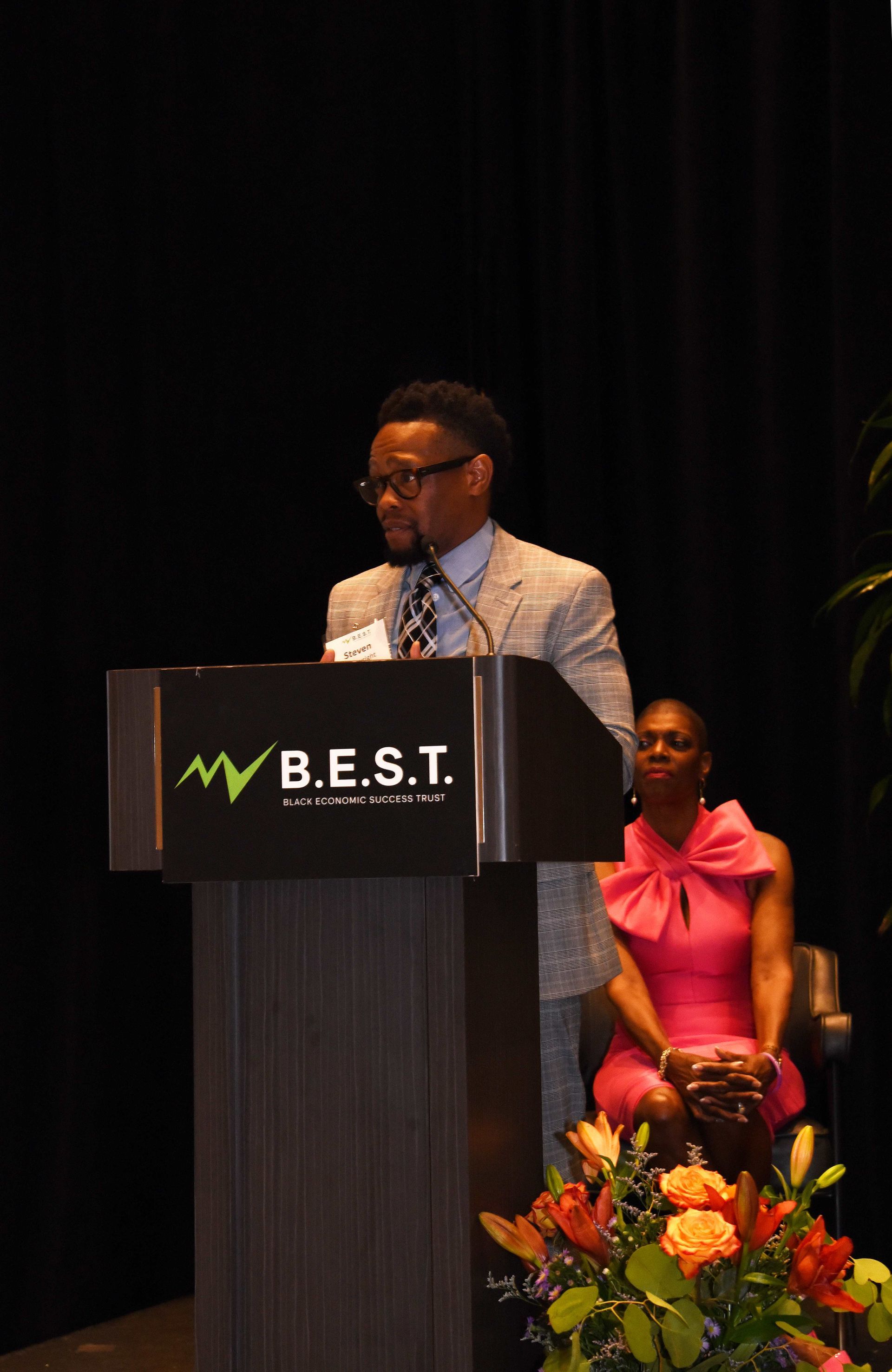 A man stands behind a podium that says b.e.s.t.