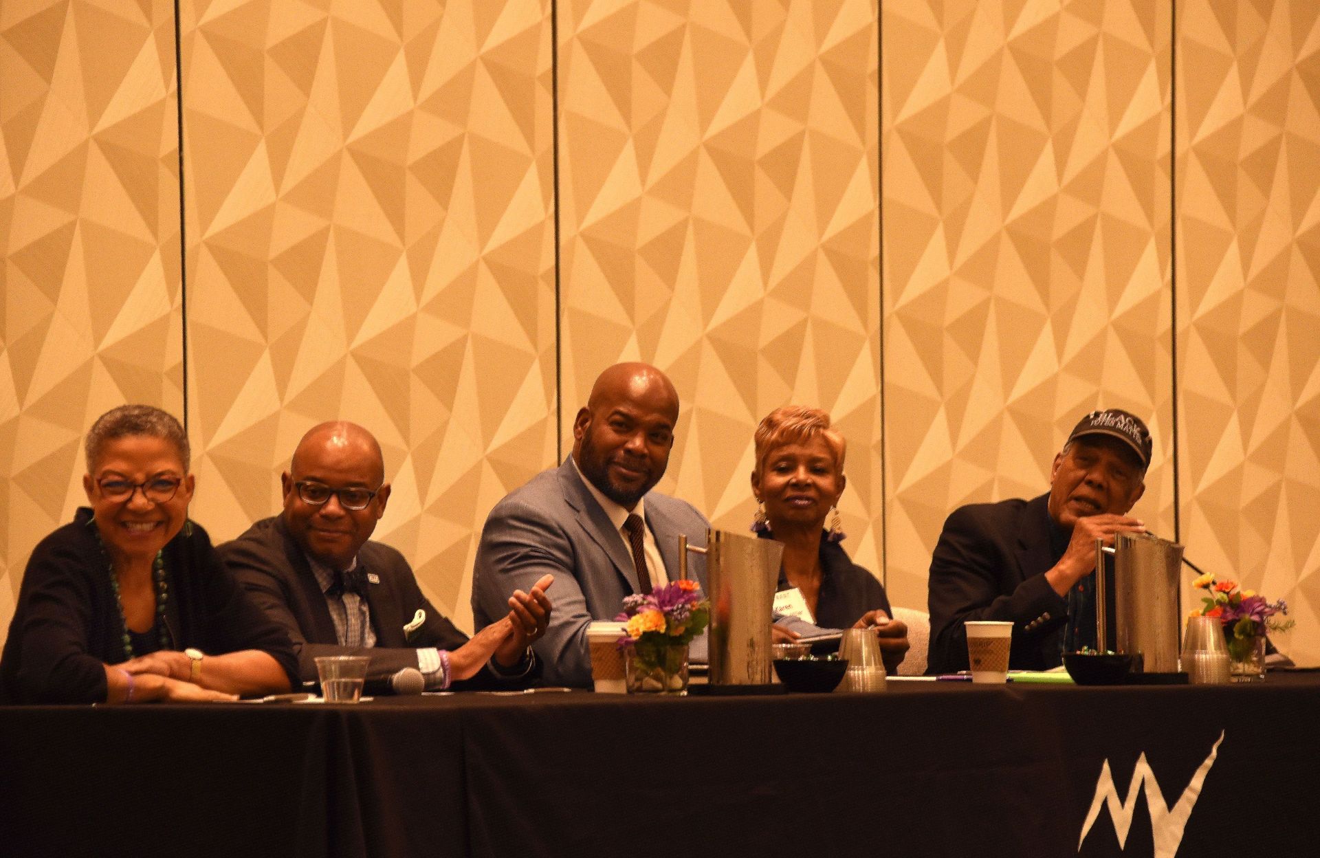 A group of people are sitting at a table in front of a wall.