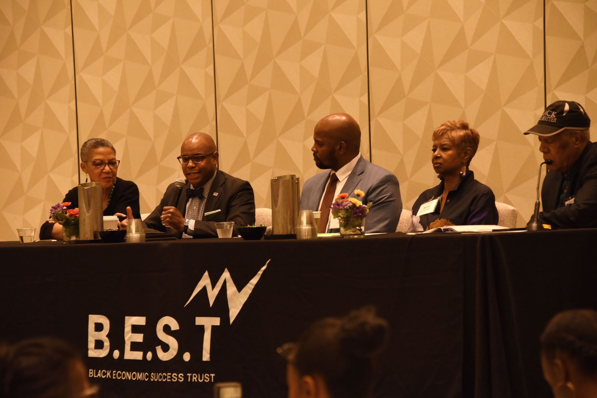 A group of people are sitting at a table in front of a sign that says b.e.s.t.