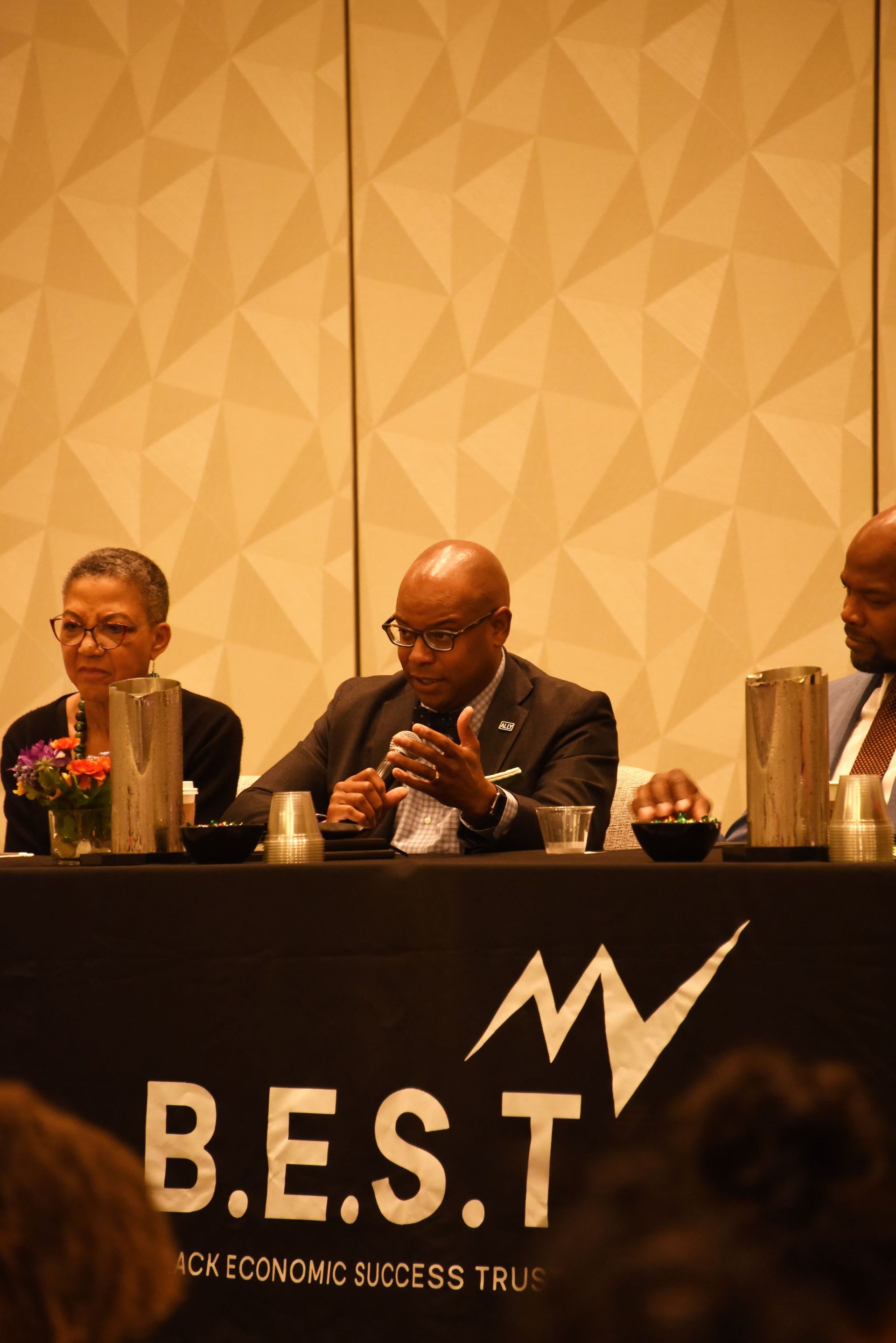 Three men are sitting at a table with a sign that says b.e.s.t.