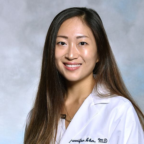 A woman wearing a white lab coat with jennifer ahn md written on it
