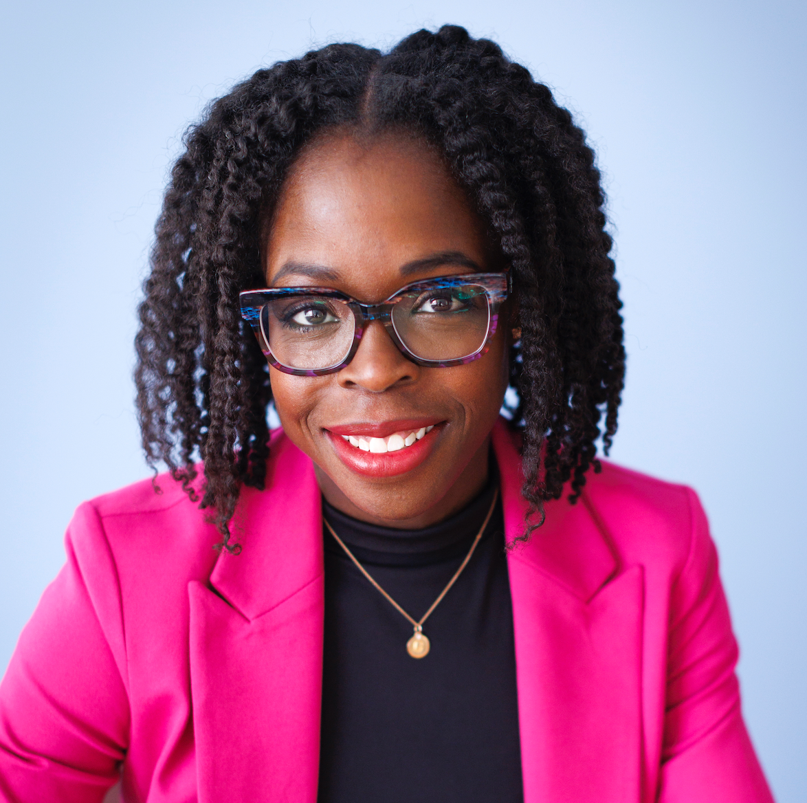 A woman wearing glasses and a pink jacket is smiling for the camera.